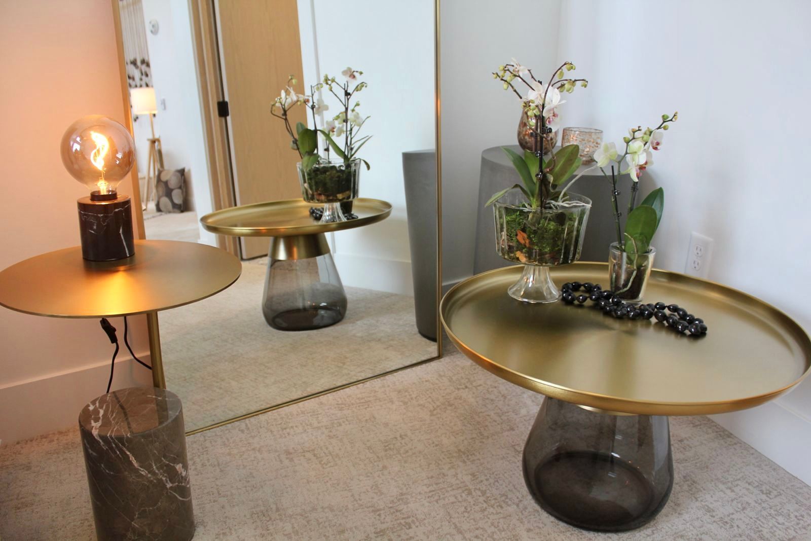 Two gold accent tables with flowers and a lamp. A large mirror reflects the scene.