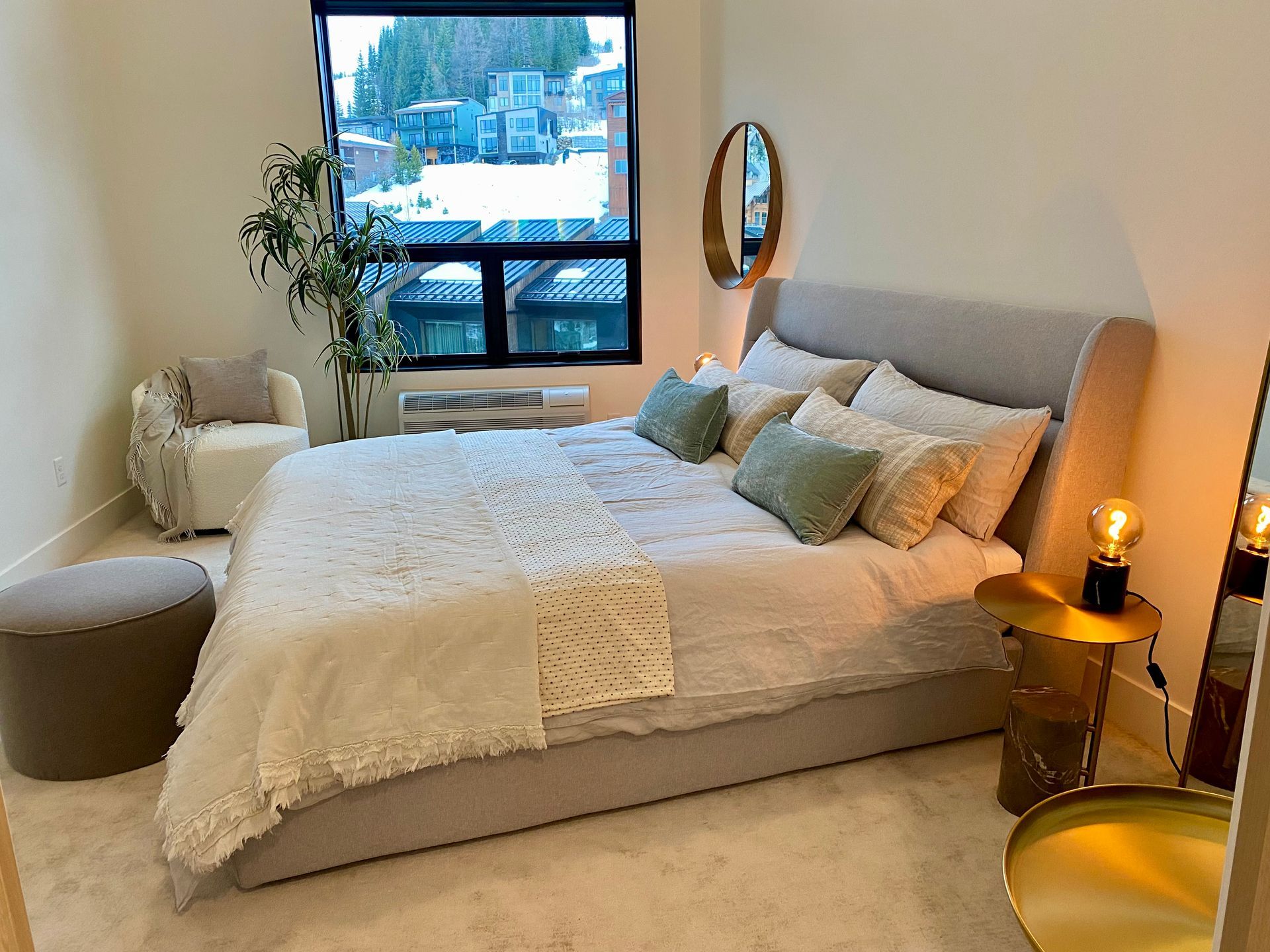 Bedroom with a bed, small chair, side table, window with a snowy view, and a mirror.