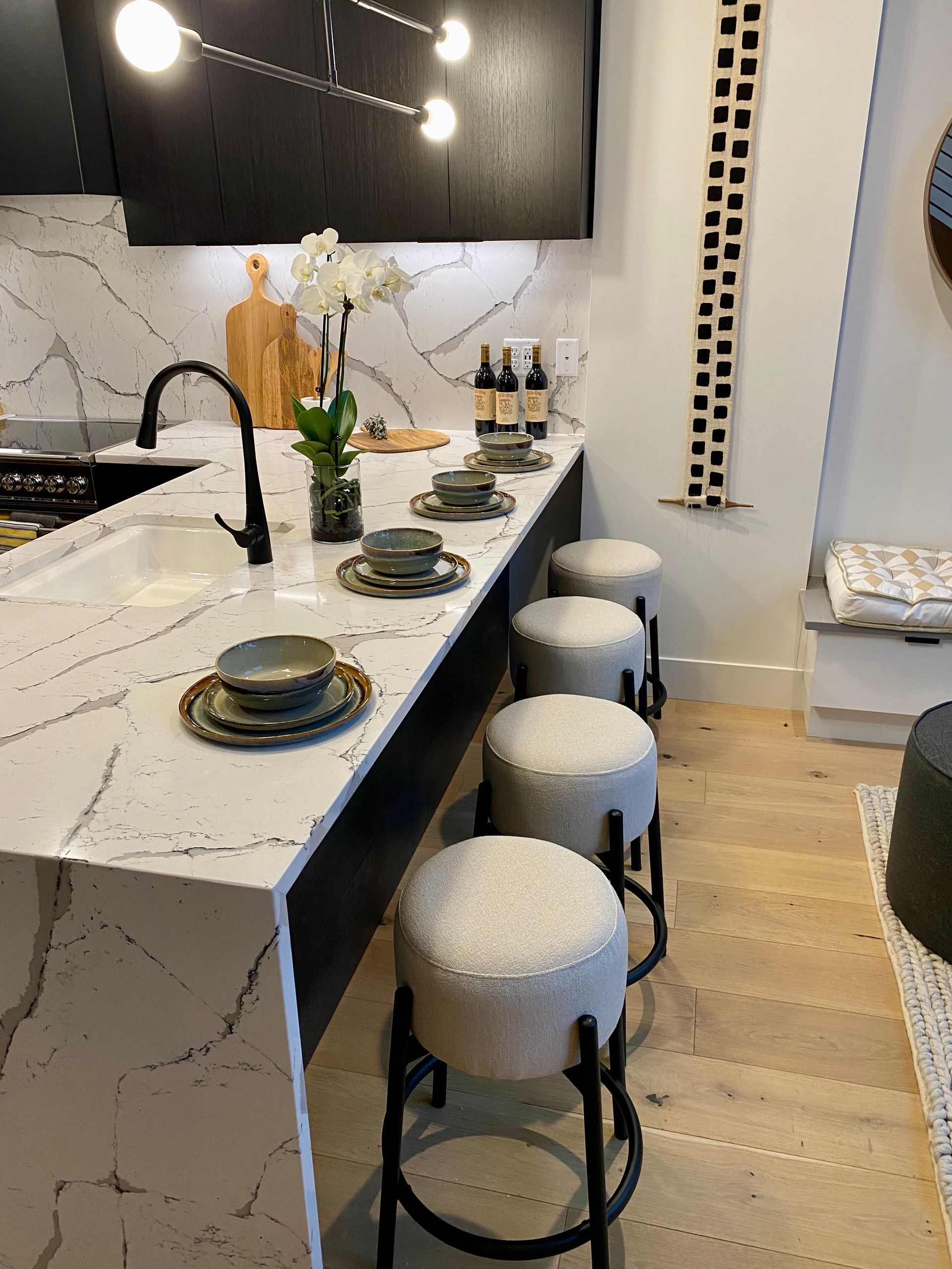 Modern kitchen with marble countertops, black stools, and overhead lighting.