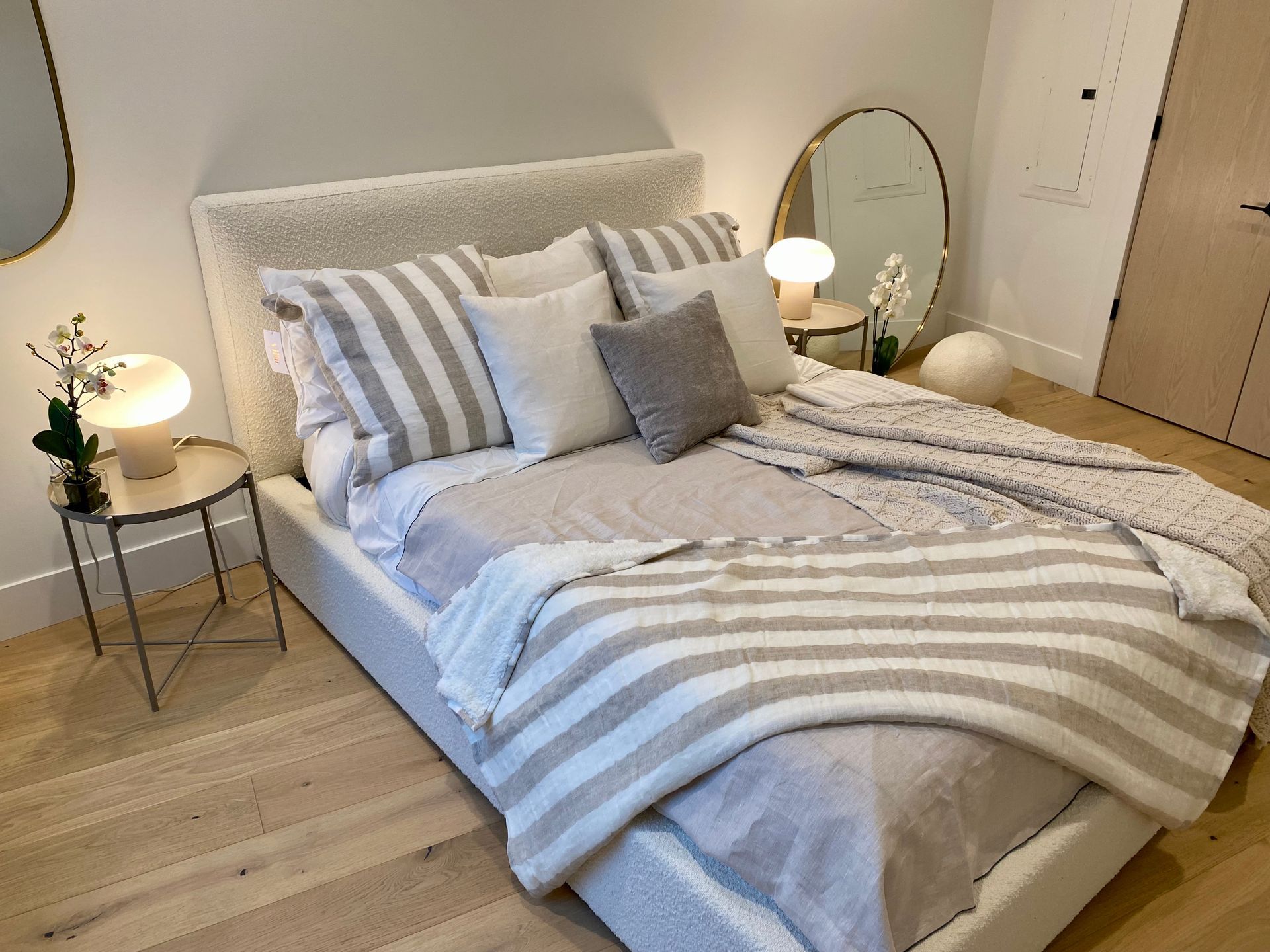 A cozy, neutral-toned bedroom with a bed covered in pillows and blankets. Two bedside tables with lamps.