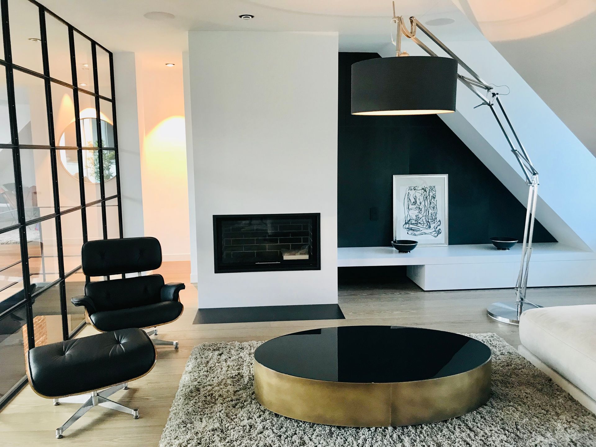 Modern living room: black leather chair and ottoman, fireplace, large lamp, round coffee table on a shag rug.