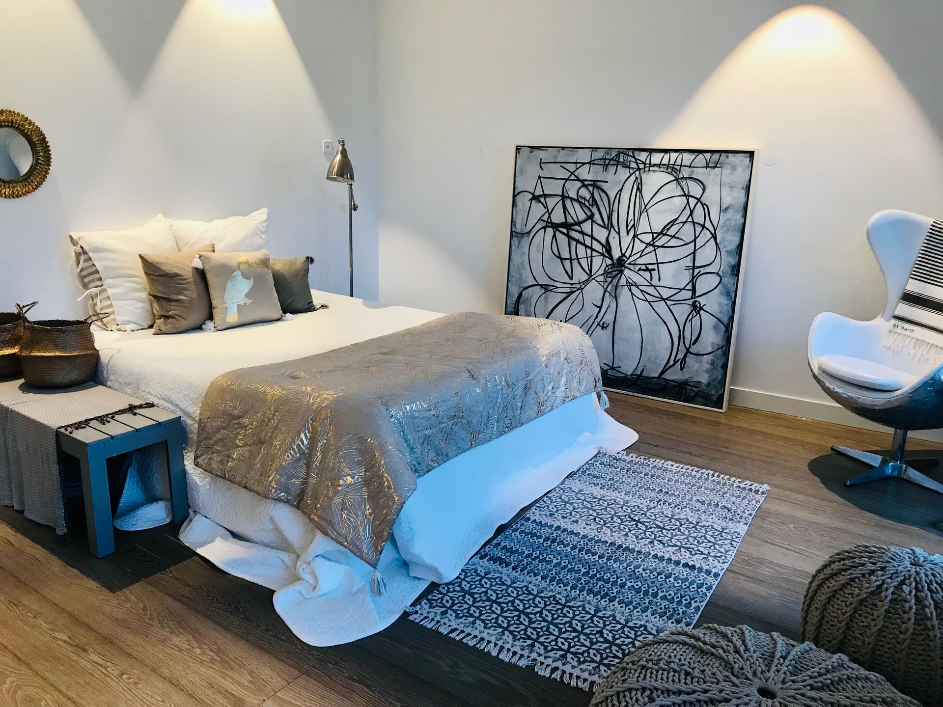 Bedroom with a bed, art, and an egg chair, featuring a neutral color palette with accent pillows and a sparkly blanket.