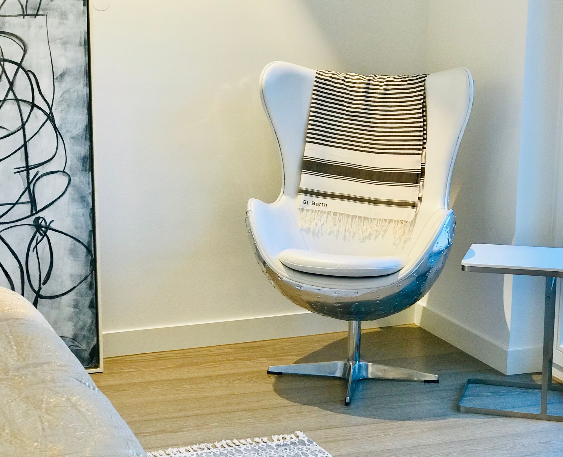 White egg chair with striped blanket, next to a small side table. Artwork on the left.