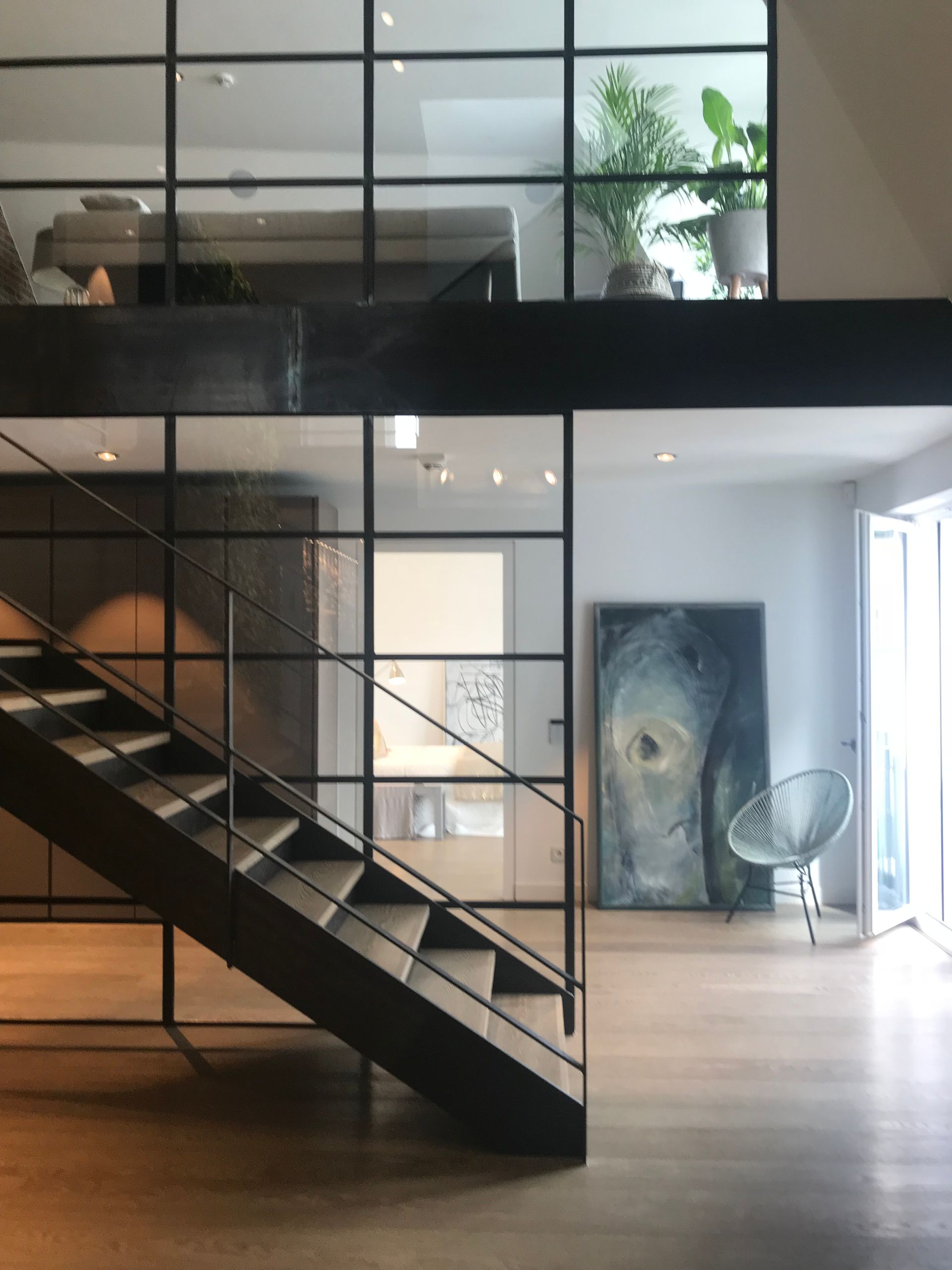 Modern interior with staircase, glass walls, and artwork; natural light and neutral tones.