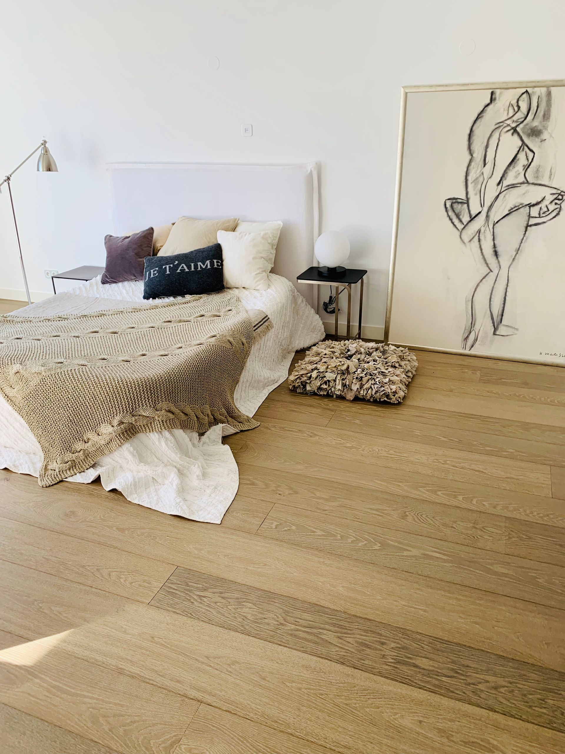 Bedroom with bed, art, and rug. Light-colored wooden floor. Soft, neutral tones create a calm atmosphere.