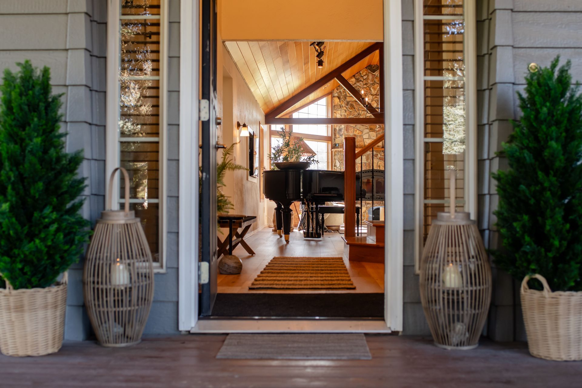 Open front doorway to a warmly lit interior with a table, chairs, and potted plants outside.
