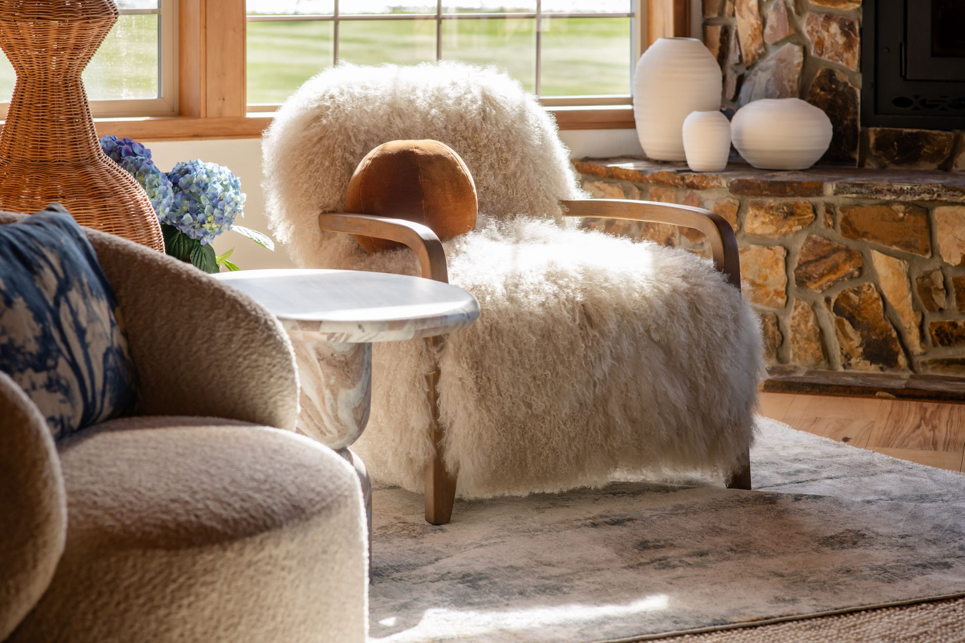 Cozy living room with shaggy chairs, a stone fireplace, and sunlight through a window