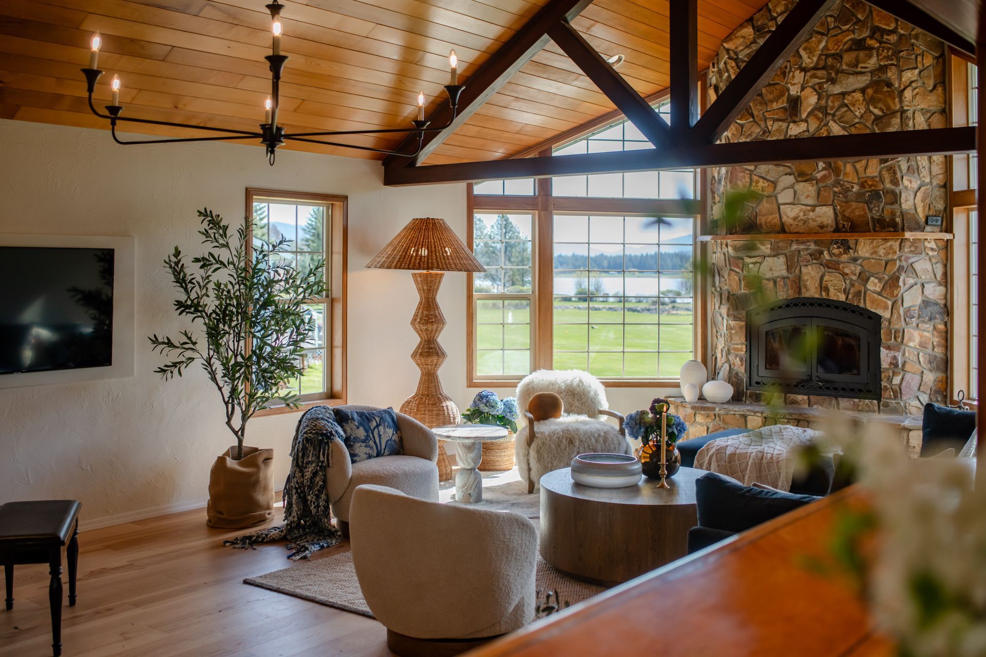 Cozy living room with exposed wood beams, stone fireplace, and large windows overlooking a field