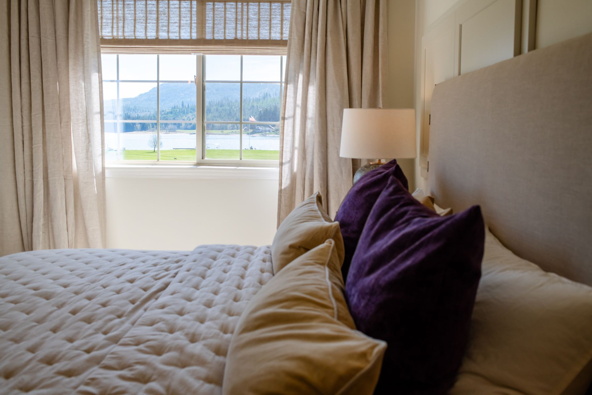 Cozy bedroom with tufted bed, purple pillows, and a window view of water and mountains