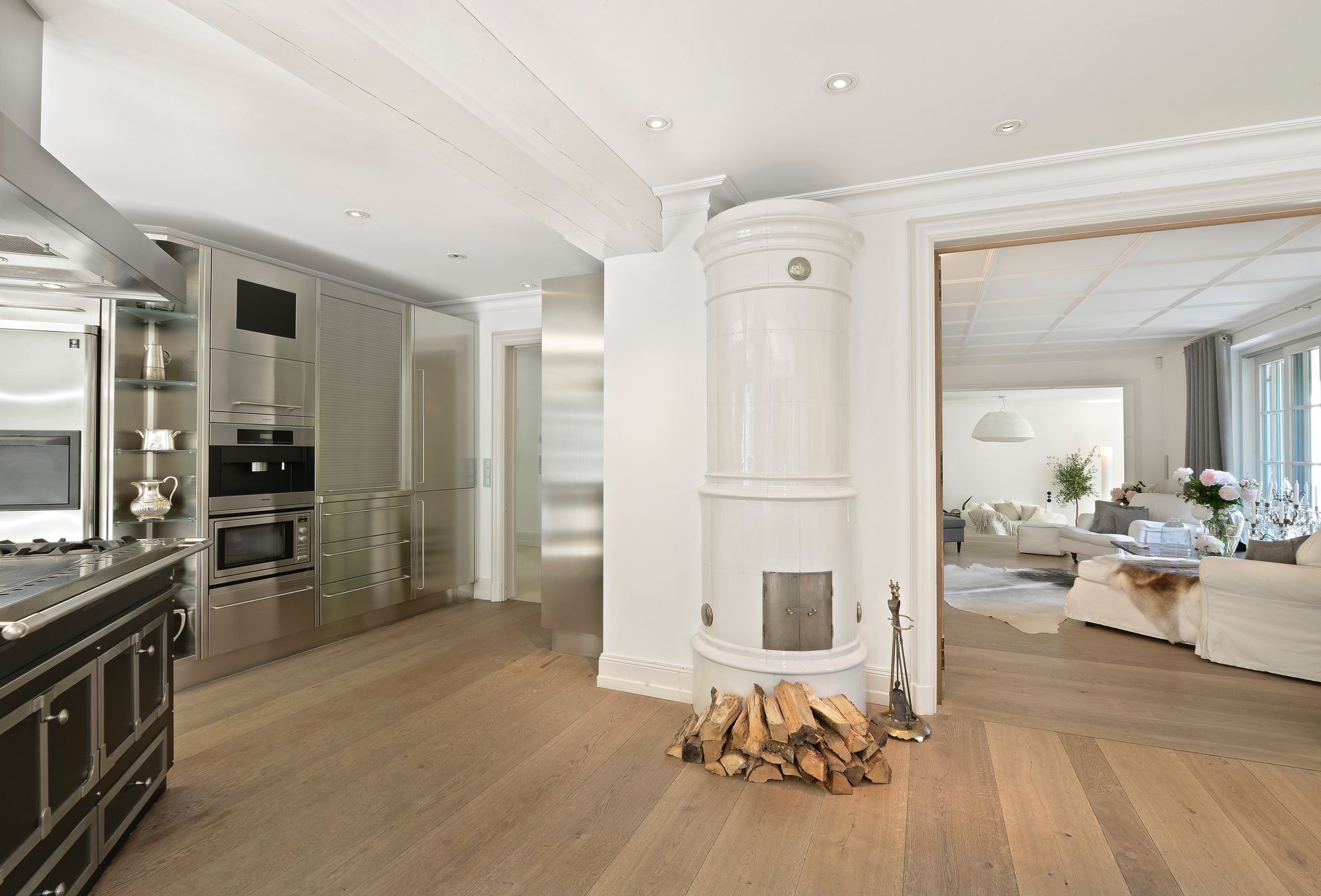 A white kitchen with stainless steel appliances, a wood-burning stove, and a view into a living room.