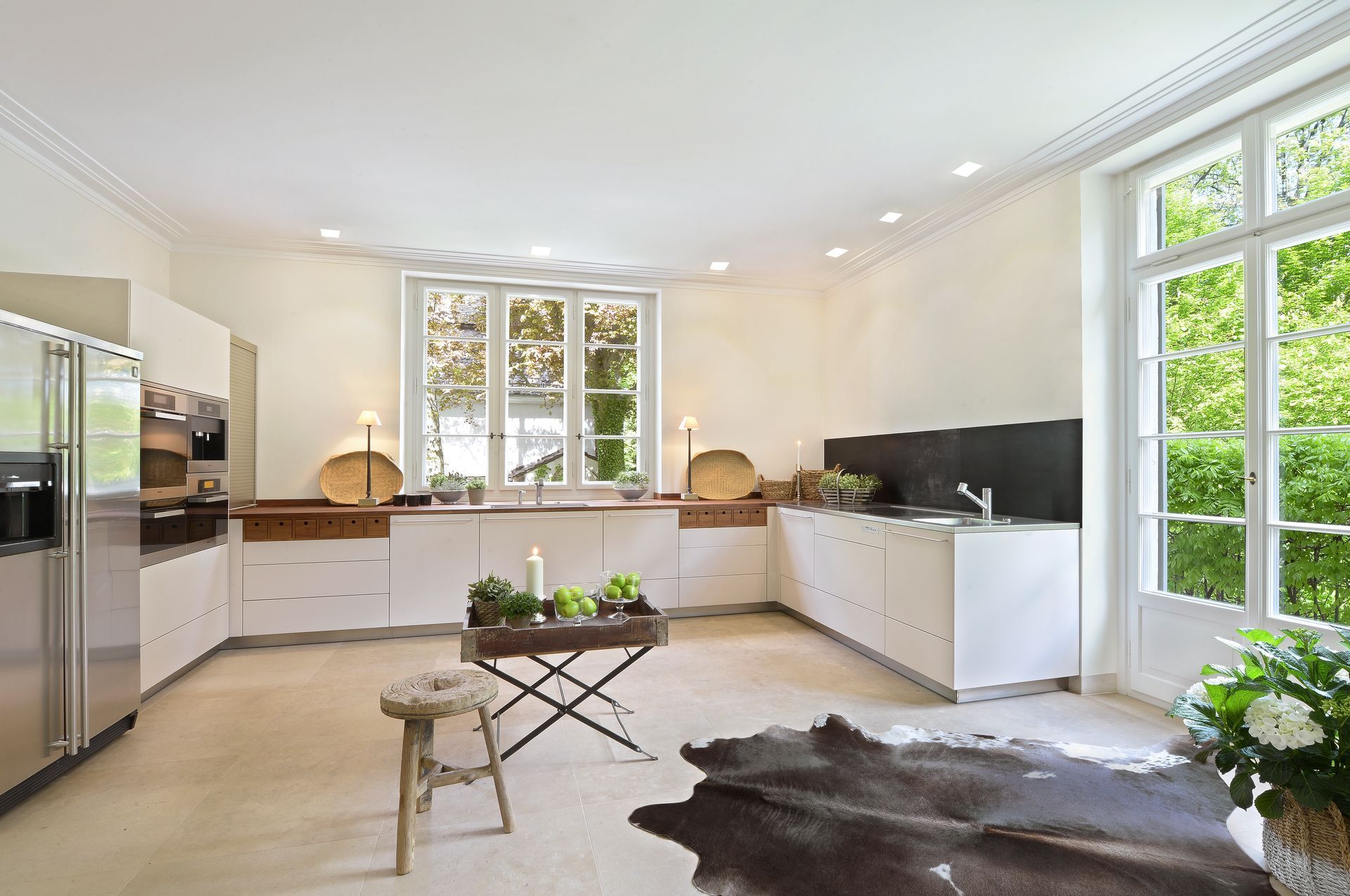 Modern white kitchen with a stainless steel refrigerator, white cabinets, and large windows.