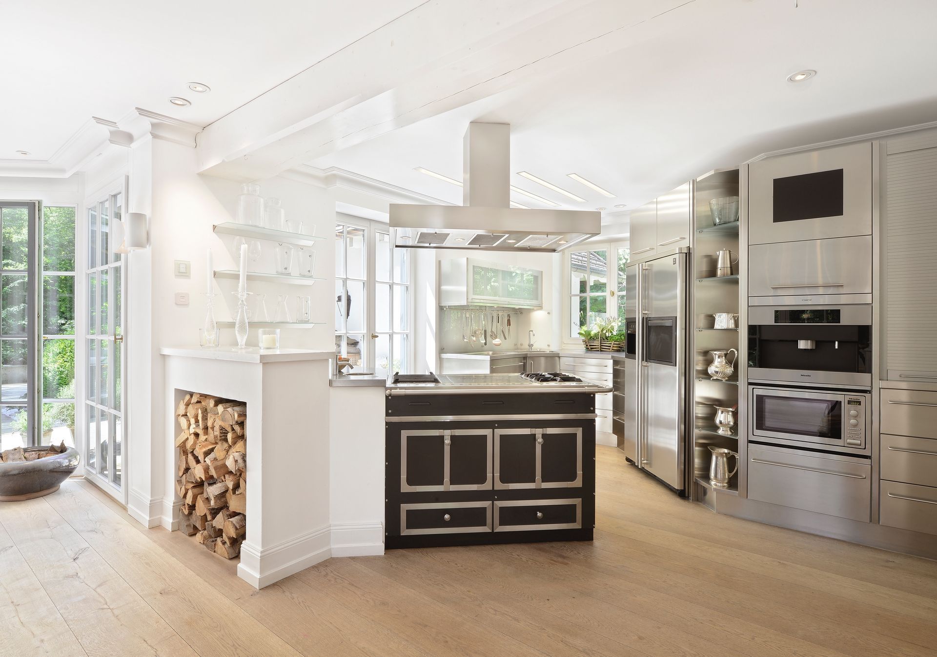 Bright, modern kitchen with stainless steel appliances, black stove, and firewood storage.