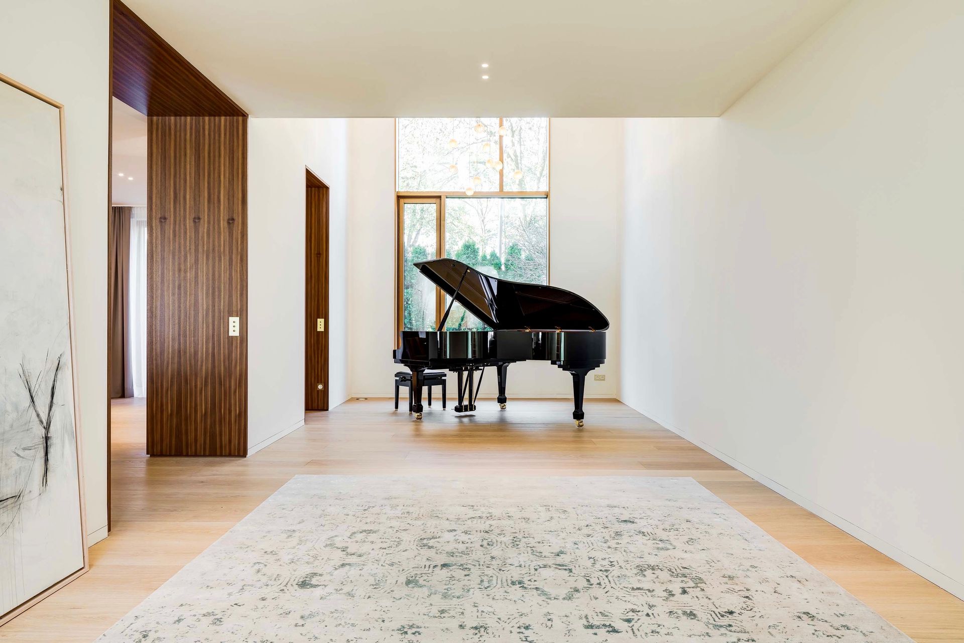 Grand piano in a bright room with light wood floors and a large window.