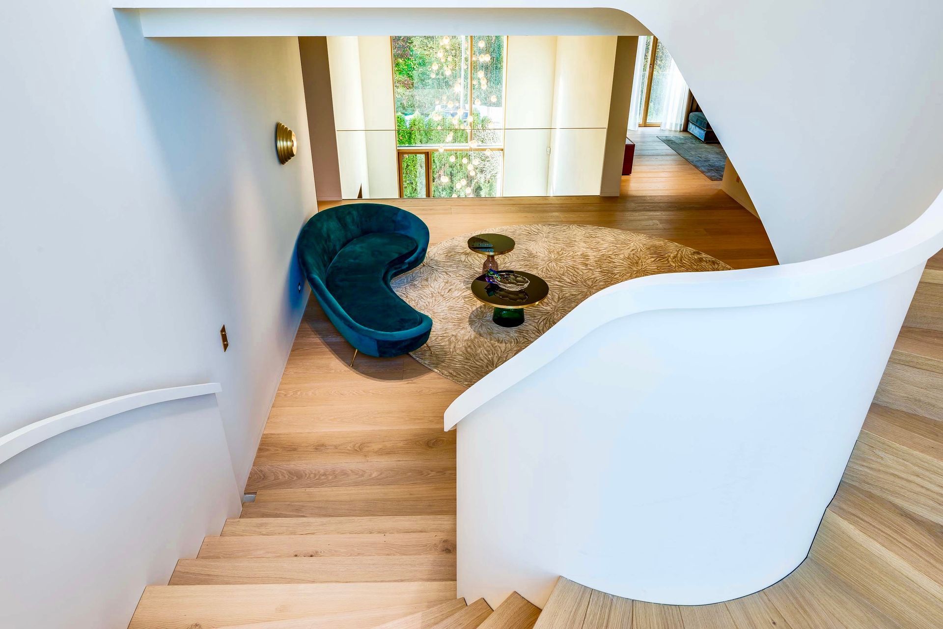 A winding staircase leads to a sitting area with a blue couch, coffee table, and a round rug.