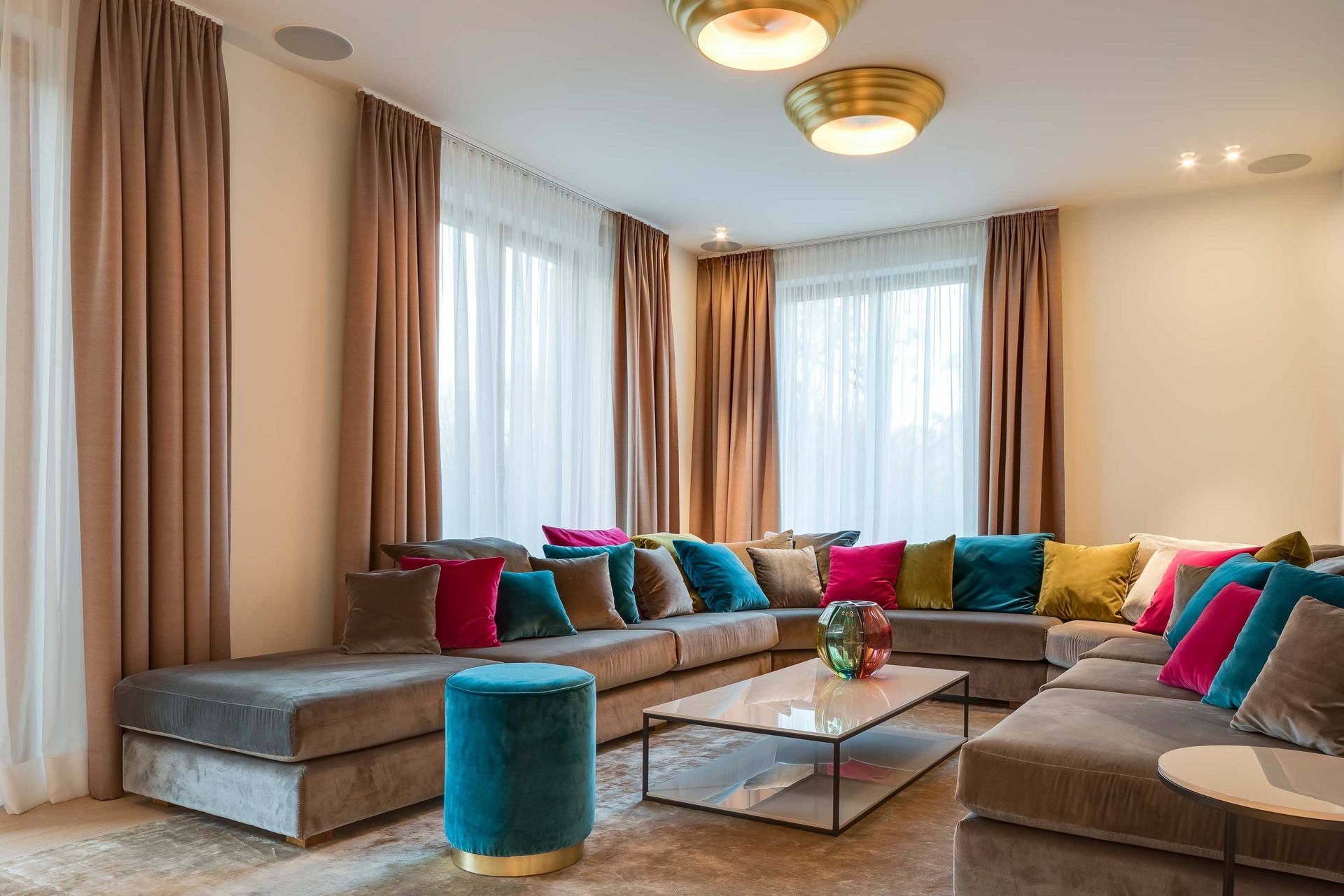 Living room with a large gray sectional sofa, colorful pillows, curtains, and a glass coffee table.