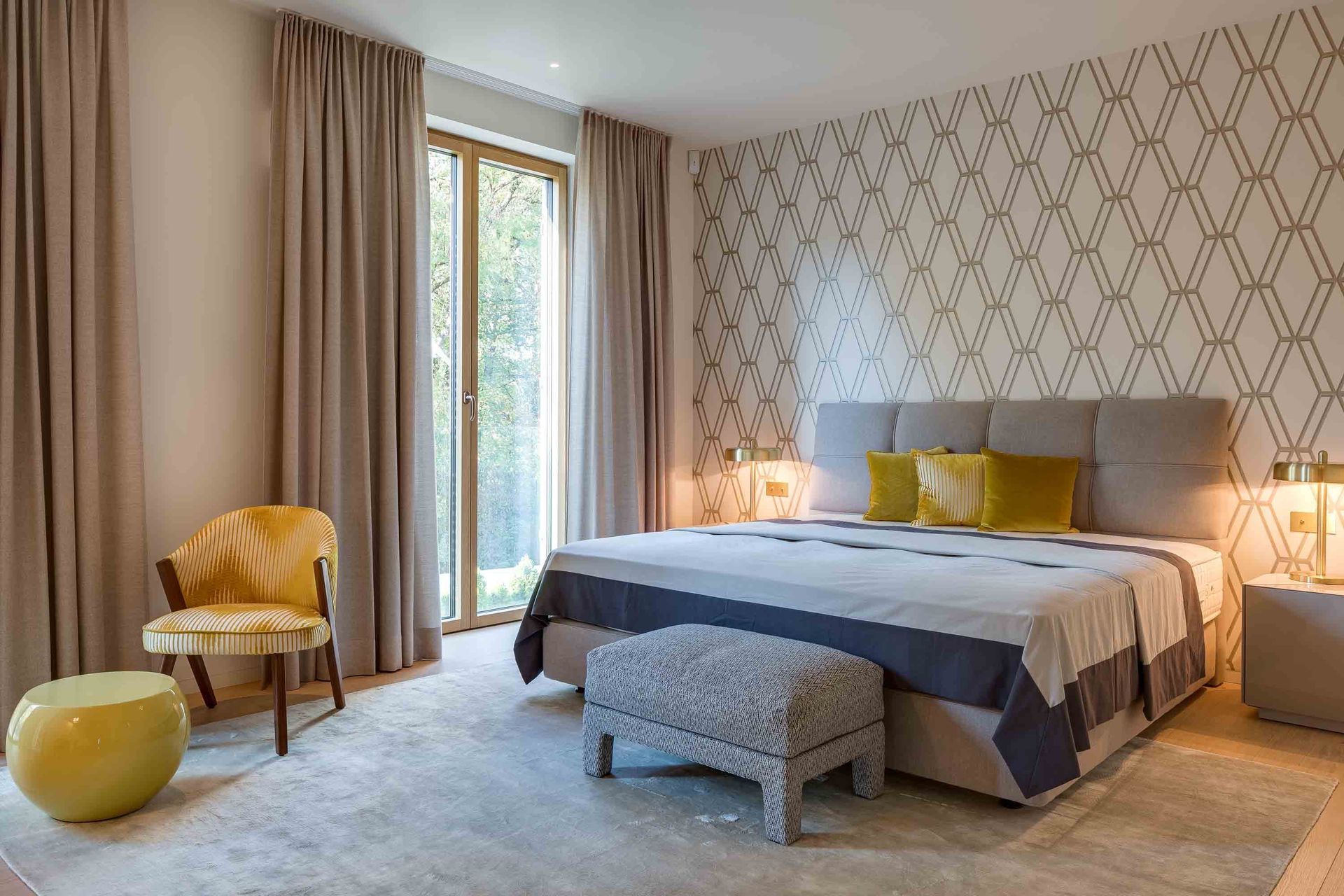 Bedroom with bed, patterned wallpaper, yellow chair, and floor-to-ceiling window with curtains.