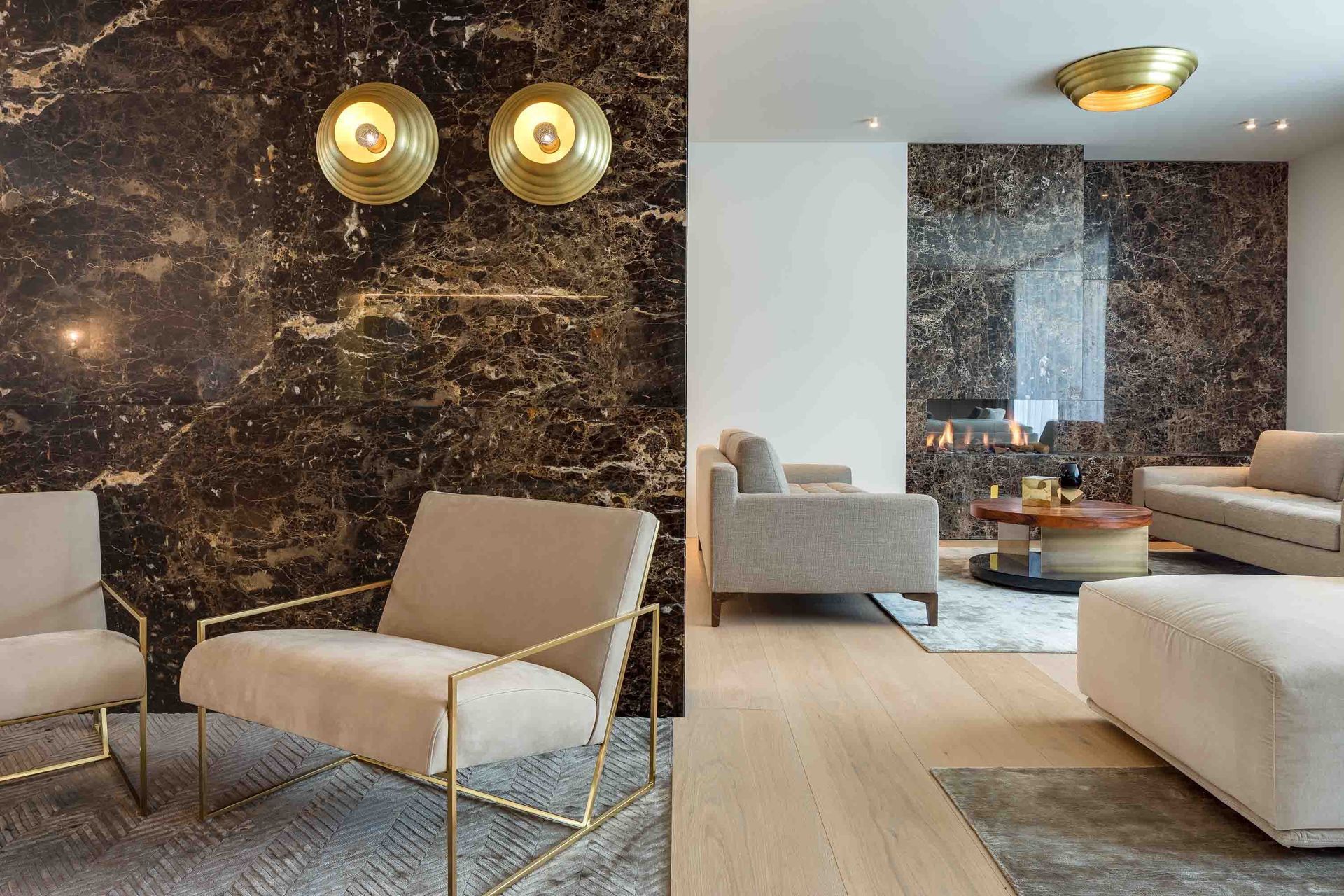 Luxurious living room: marble walls, gold accents, cream furniture. Two armchairs, sofa, fireplace, and light fixtures.