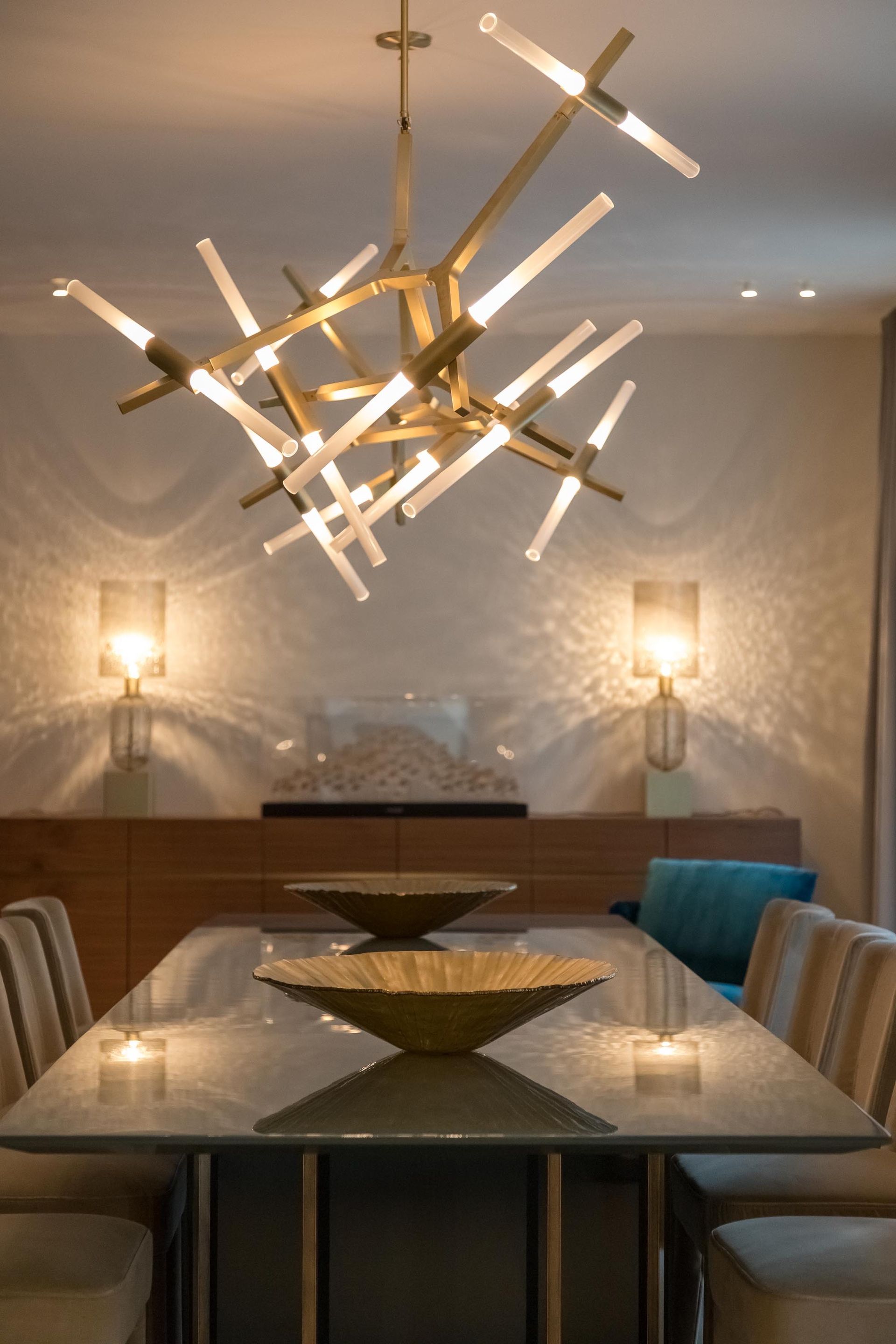 Dining room with modern chandelier over a table set with bowls; sconces on the wall.