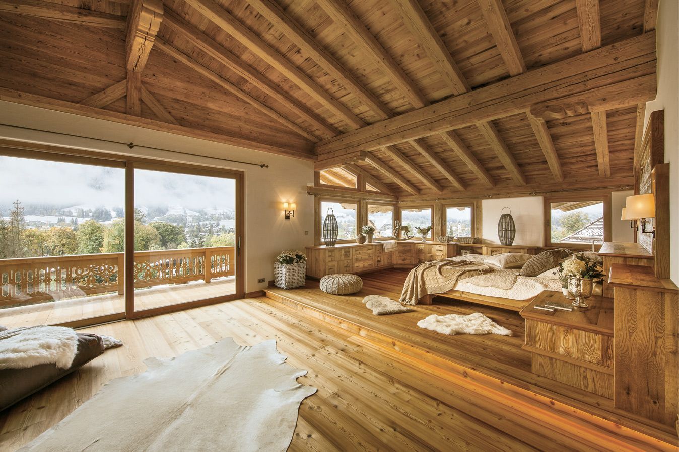Spacious wooden-floored bedroom with vaulted ceiling, large windows, balcony, and mountain view.