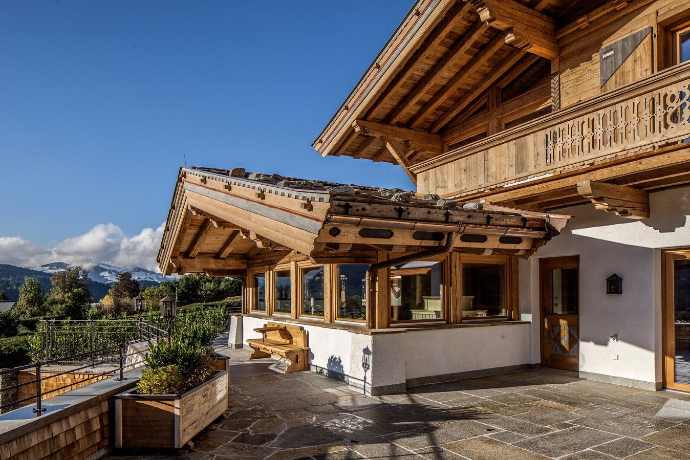 Wooden chalet with a covered patio, featuring a view of mountains and blue sky.