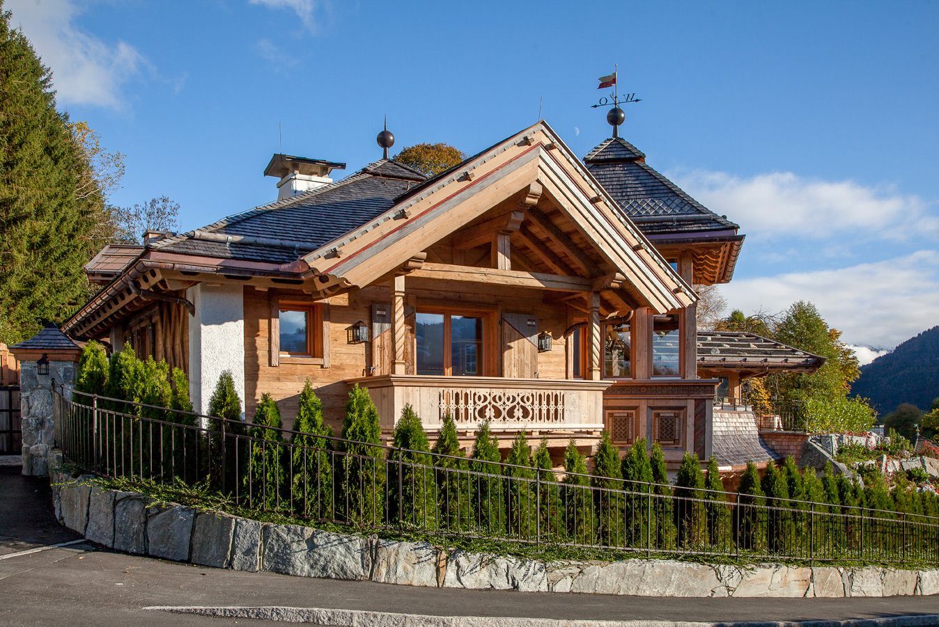 Wooden chalet with dark roof, small balcony, and stone fence under a blue sky.