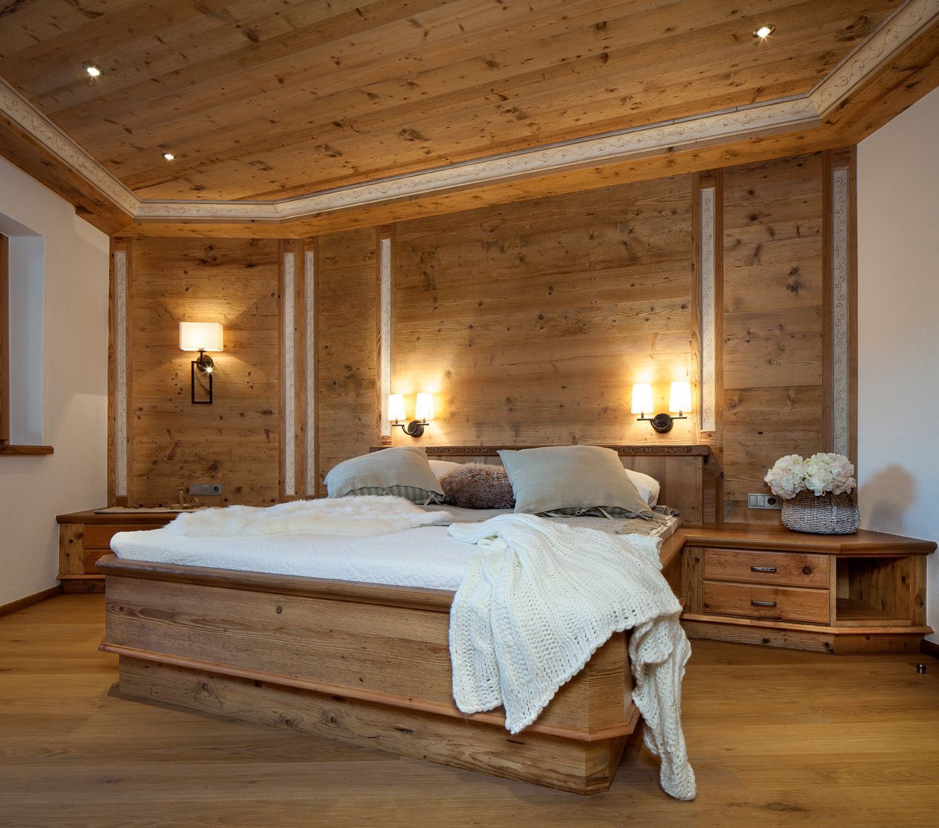 Wooden bedroom with bed, bedside tables, and wall paneling; warm lighting.