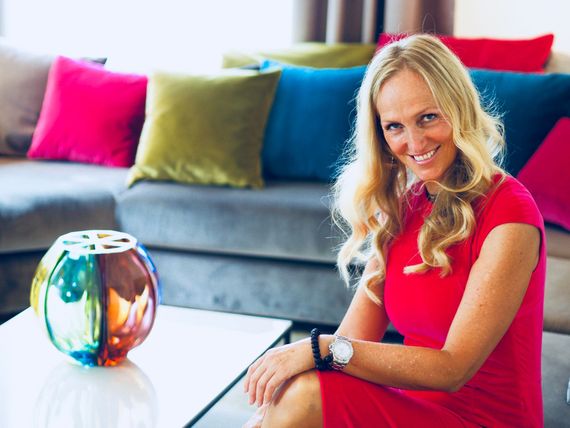 Michaela Jansen - Certified Expert Woman in red dress smiles, seated near colorful couch and glass art.