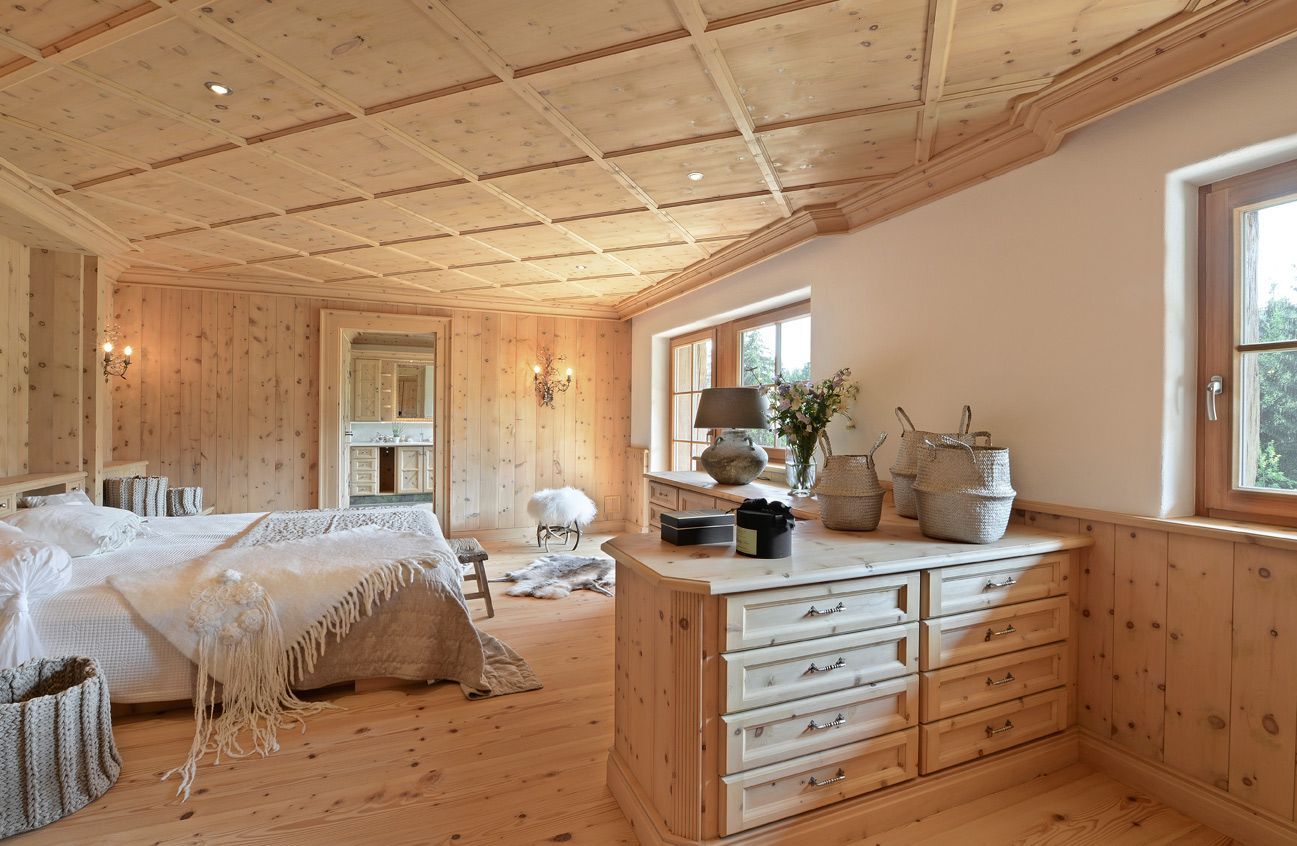 Bright, wood-paneled bedroom with a bed, dresser, and windows; natural light streams in.