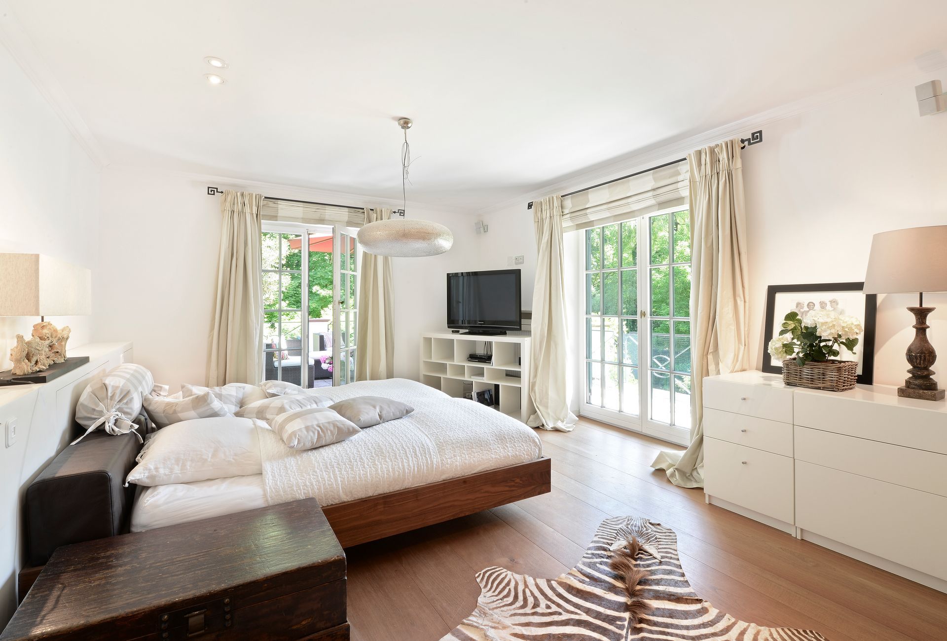 Bedroom with a bed, white furniture, sliding glass doors to a balcony, and a zebra rug.