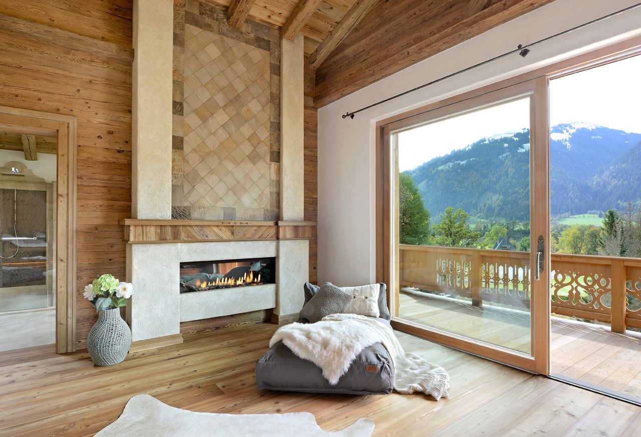 Cozy living room with fireplace, wood paneling, large windows overlooking mountains and balcony.