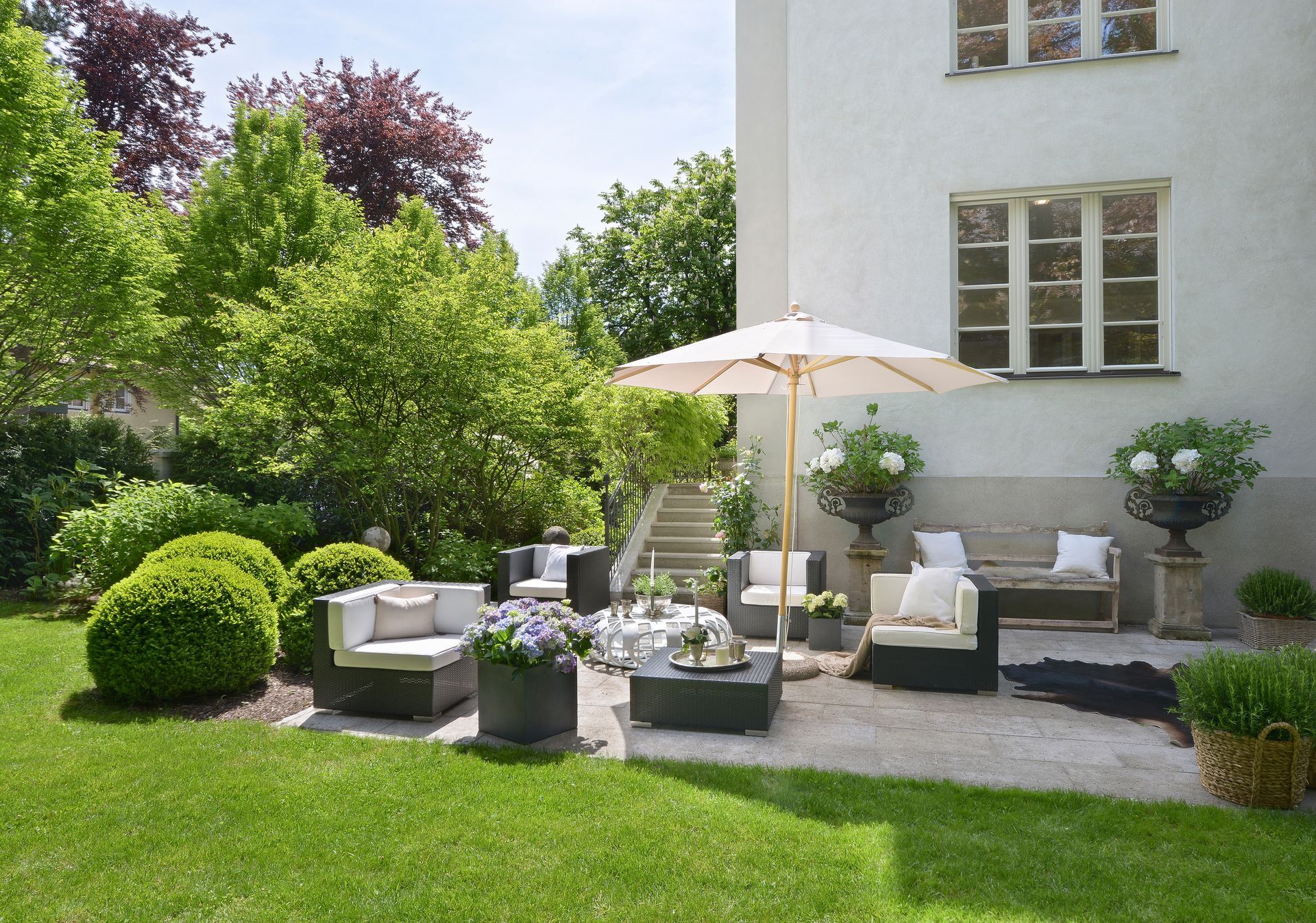 Patio with outdoor furniture, umbrella, and a building in a garden setting.