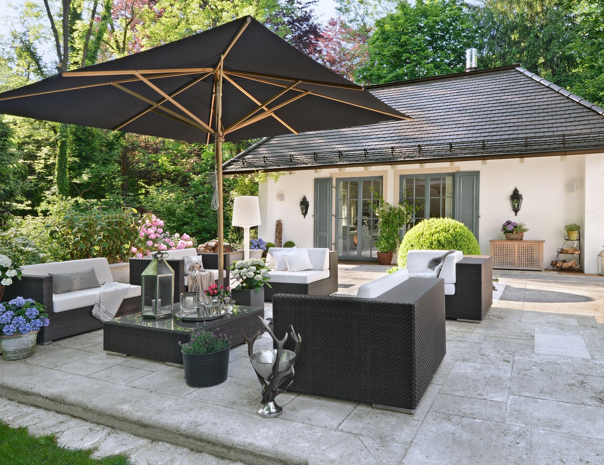 Patio with dark wicker furniture, black umbrella, and white house with shutters.