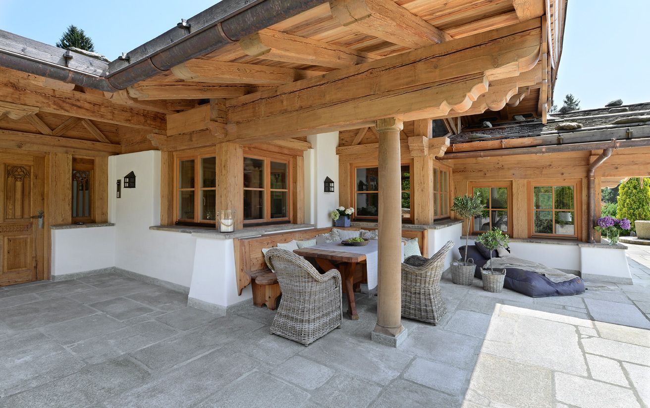 Exterior of a cabin with wooden beams, porch seating, and a stone patio.