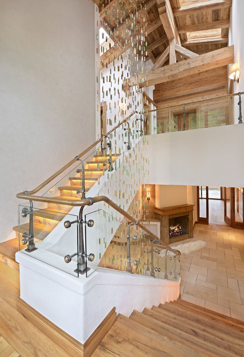 Wooden staircase with glass railing and decorative wall. Fireplace visible in background.
