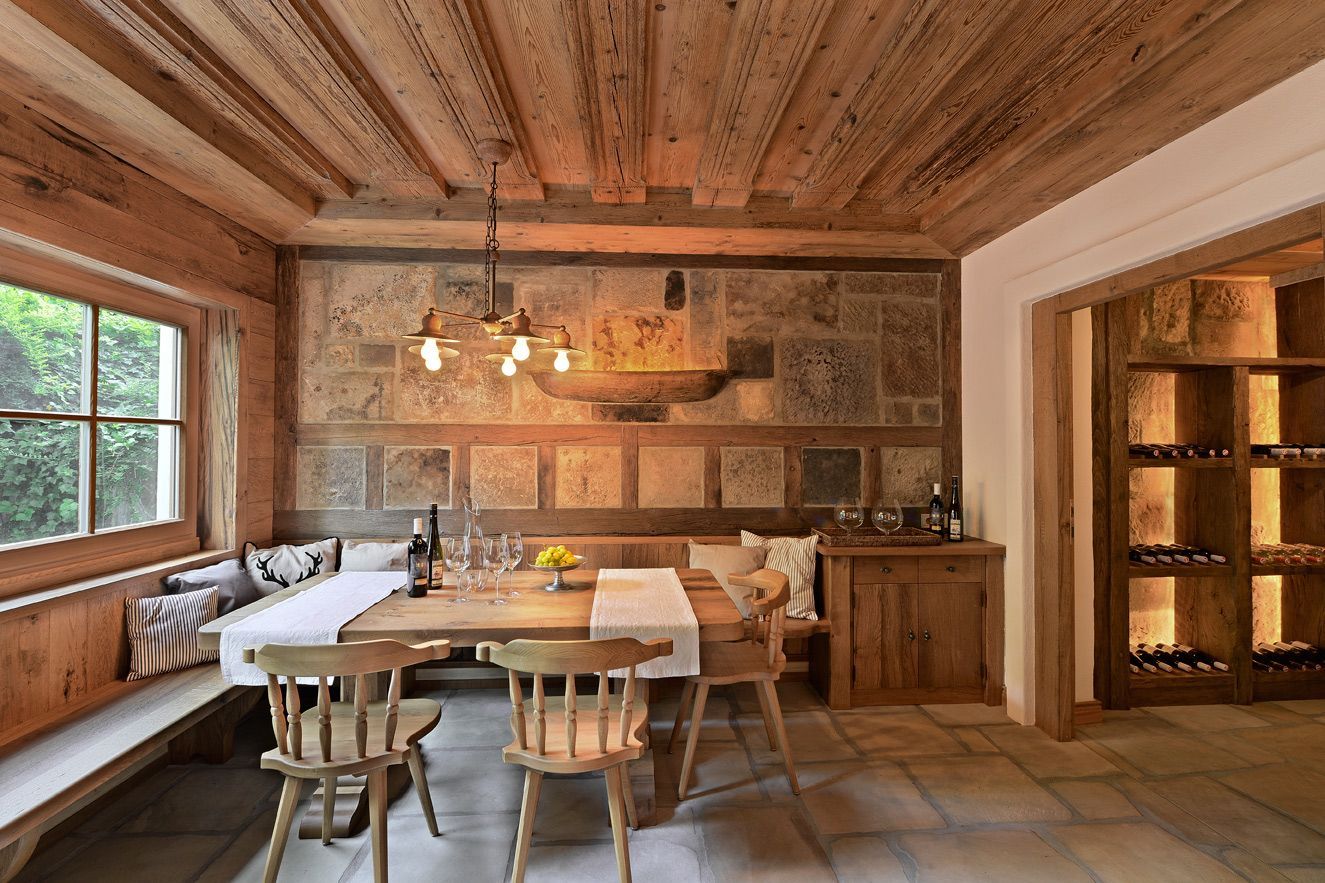 Cozy dining room with wood ceiling and paneling, stone wall backdrop, table set for dining, bench seating.