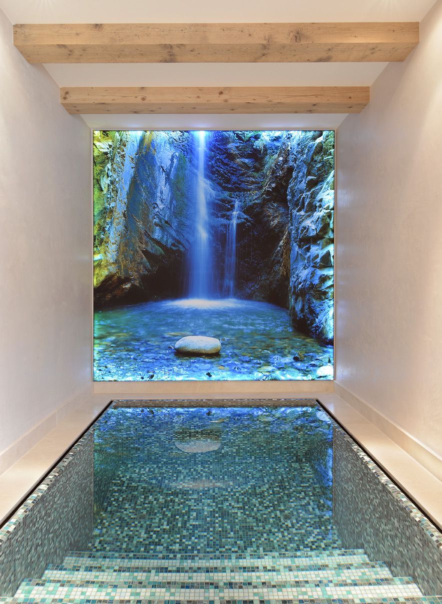 Pool with glass tile and waterfall image on the wall, under wooden beams.
