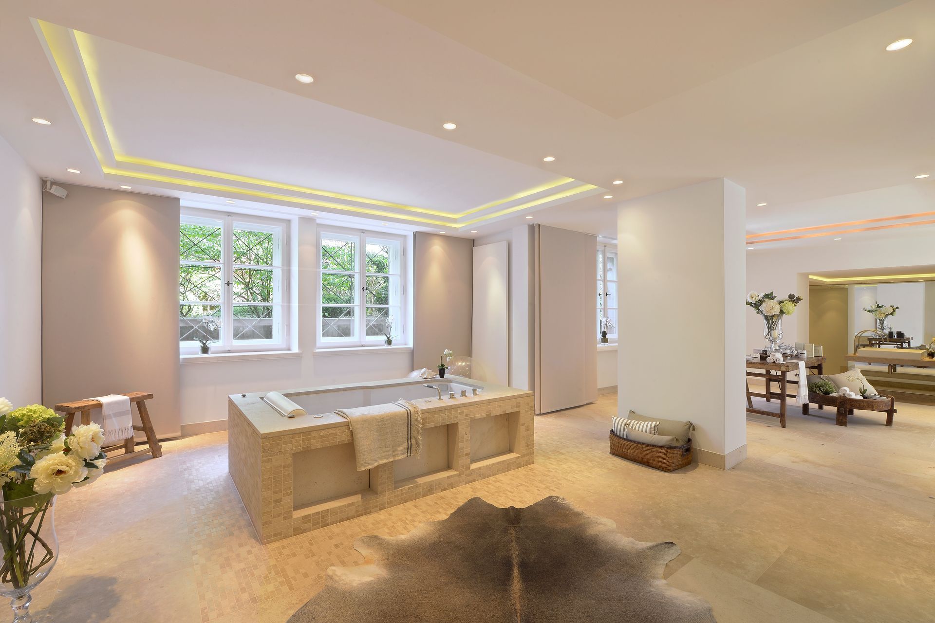 Spacious, bright bathroom with stone tub, three windows, hardwood floor, and cowhide rug.