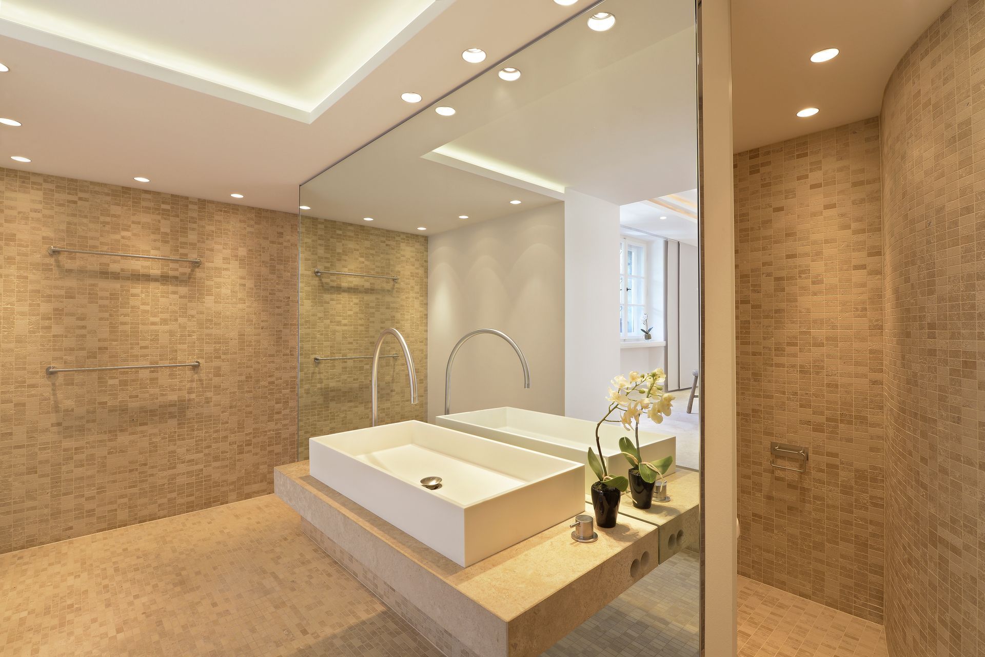 Modern bathroom with neutral-toned tiled walls and floors, large mirror, and white rectangular sink.