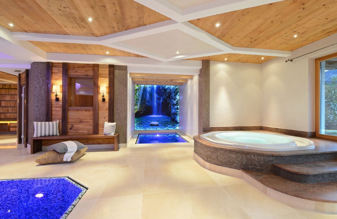 Spa with jacuzzi and pool, wood and stone accents, ceiling lights, and waterfall view.