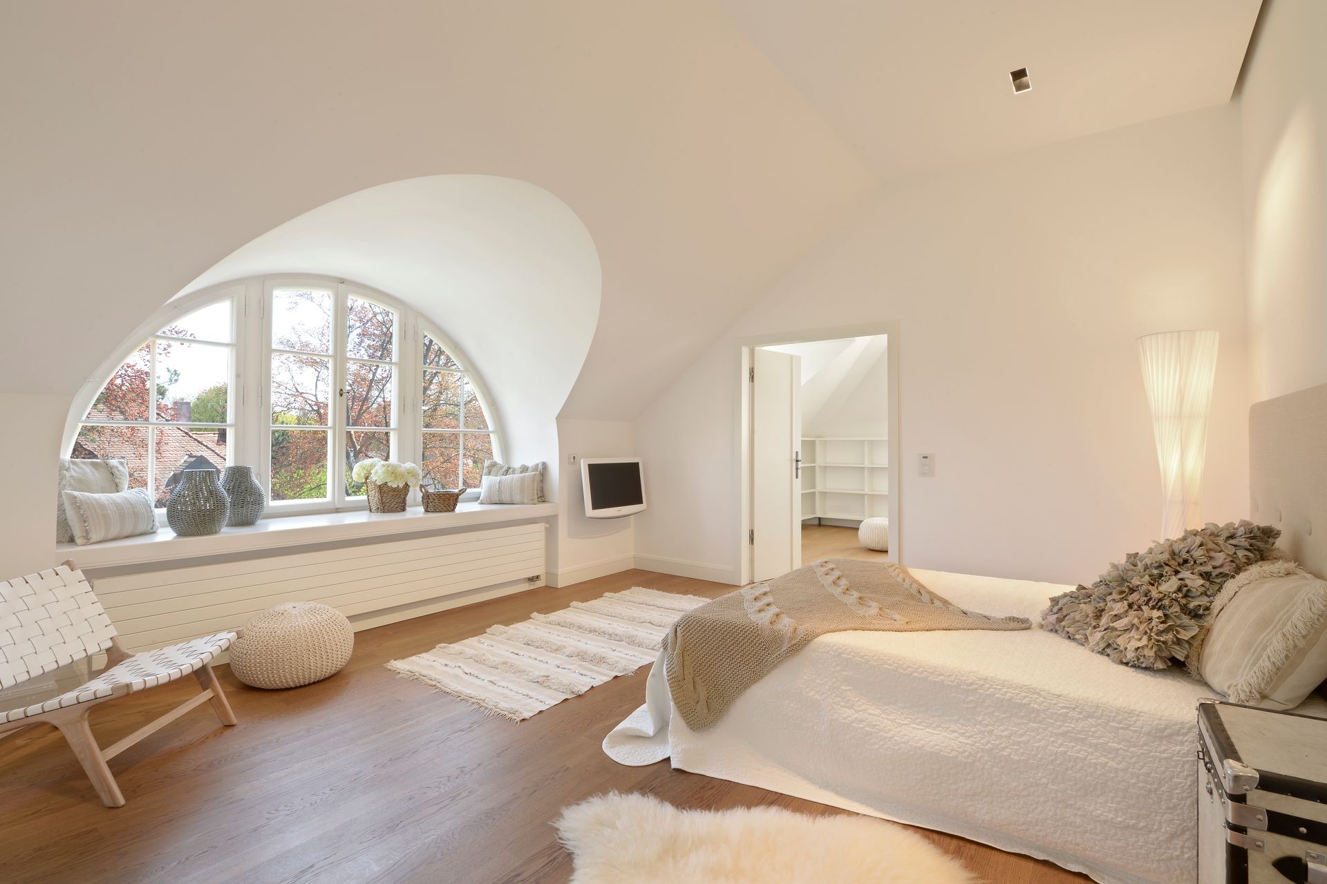 White bedroom with arched window, bed, and sitting area.