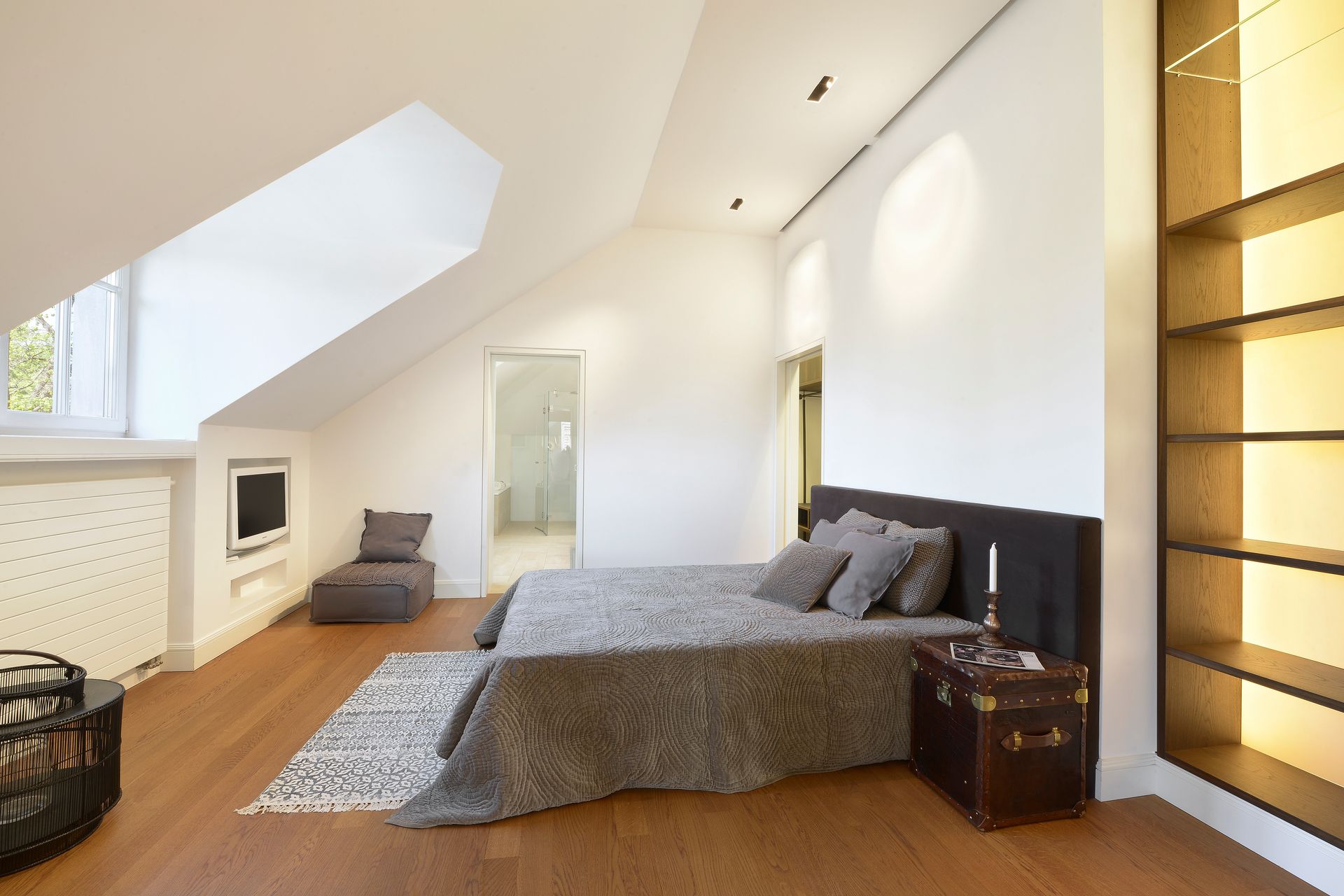 Bedroom with slanted ceiling, bed with gray bedding, wooden floor, and built-in bookshelf.