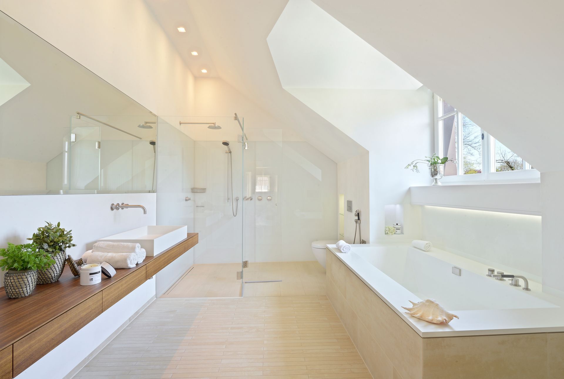 Bright, modern bathroom with white walls, skylight, and large glass shower. Wooden vanity and built-in tub.