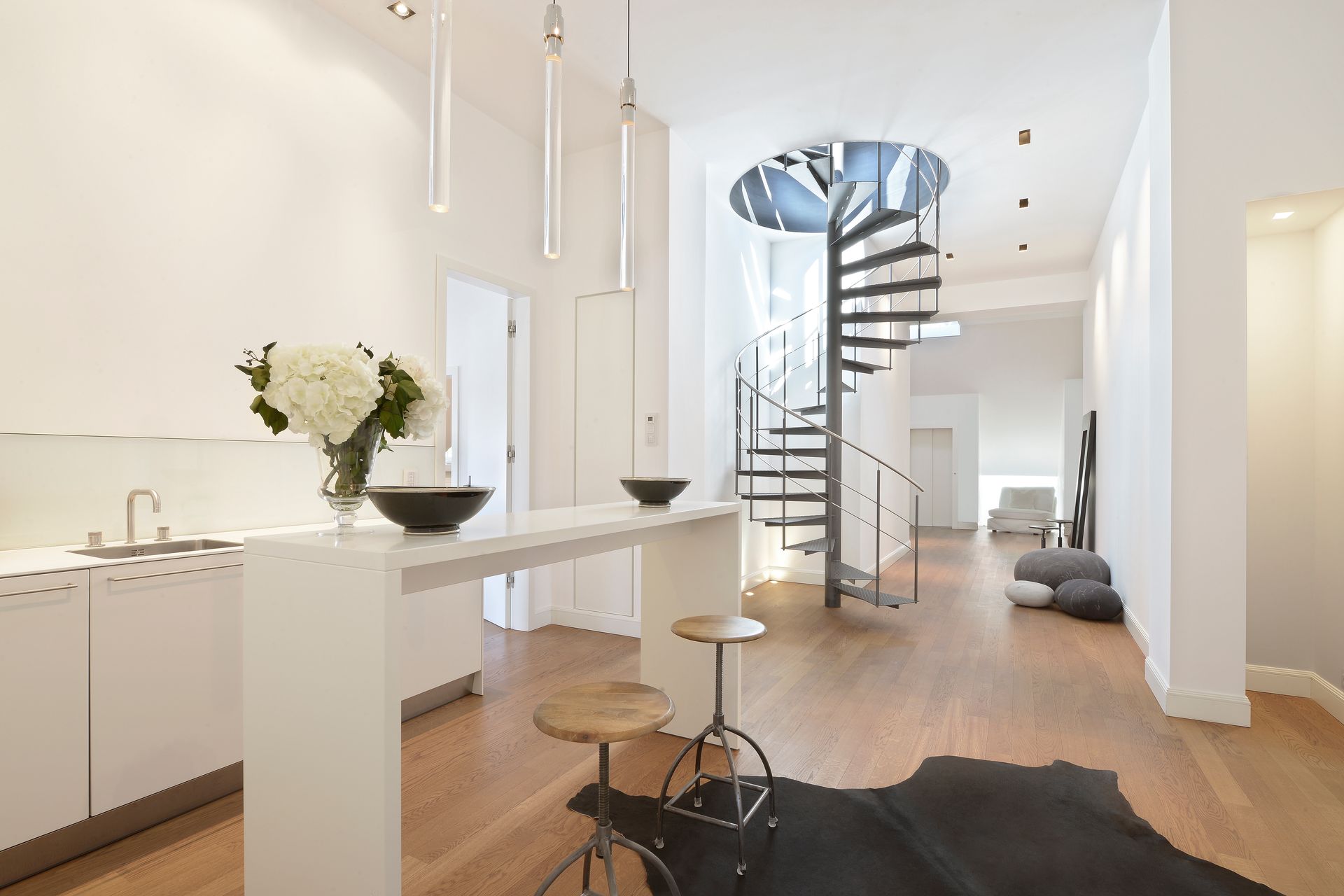Modern interior with white walls, wooden floor, spiral staircase, and kitchen island.