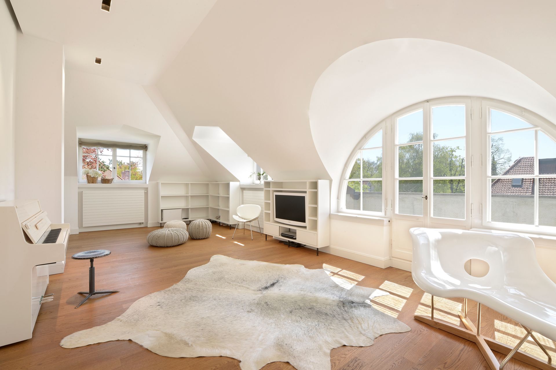 Bright, airy living room with large arched windows and white walls, a cowhide rug, and a white piano.