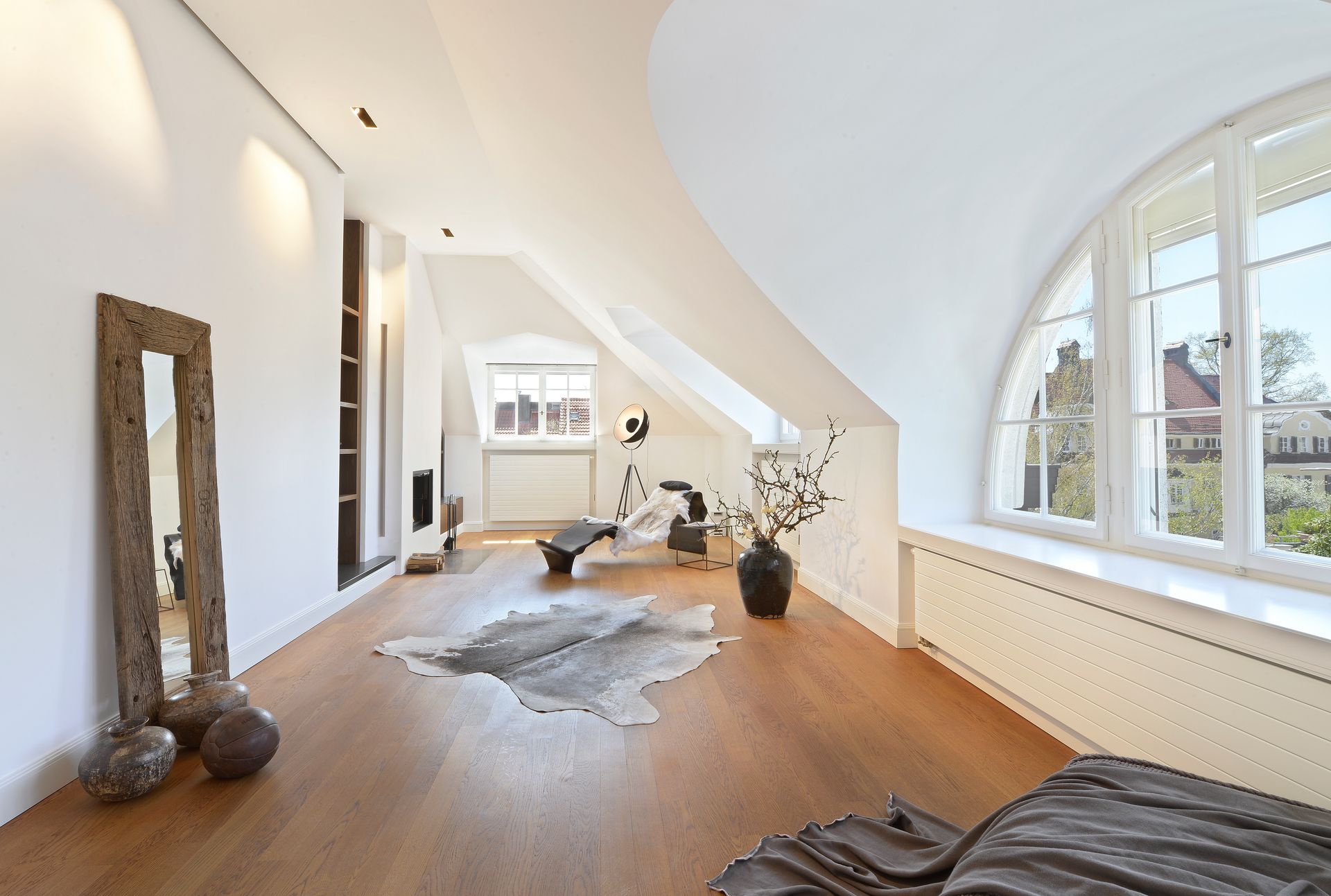 Spacious room with slanted ceiling and arched window; wooden floor, large mirror, exercise equipment.