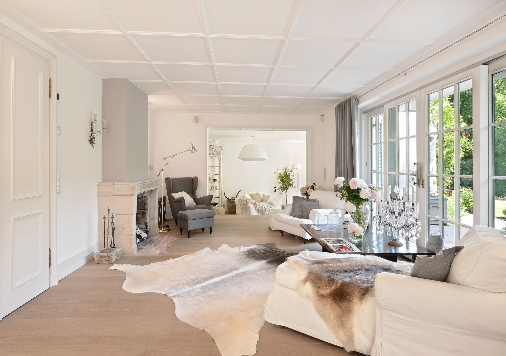 Bright living room with white walls, ceiling and large windows; light wood floor, cowhide rug, fireplace.
