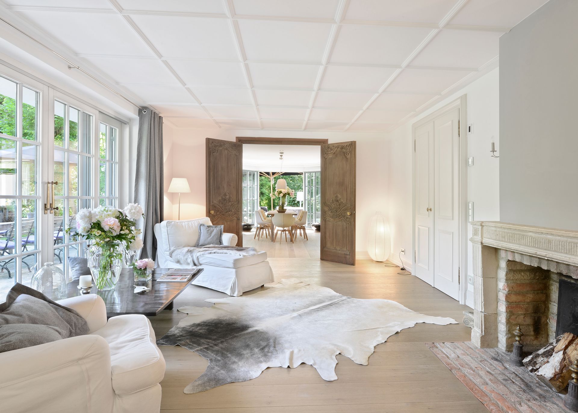 Bright, airy living room with white furniture, cowhide rug, fireplace, and French doors leading to a dining area.