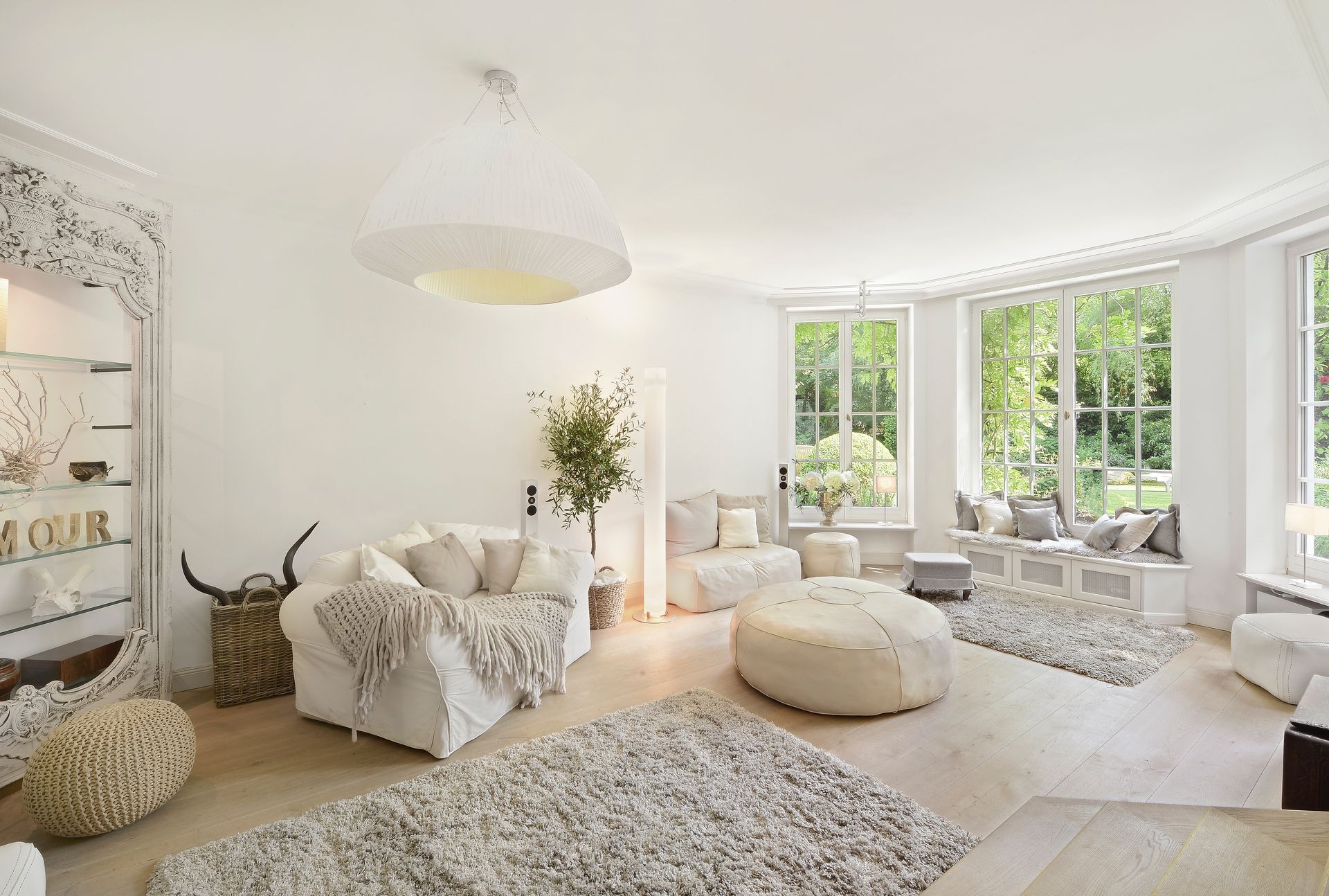 Bright white living room with neutral-toned furniture and large windows overlooking a garden.