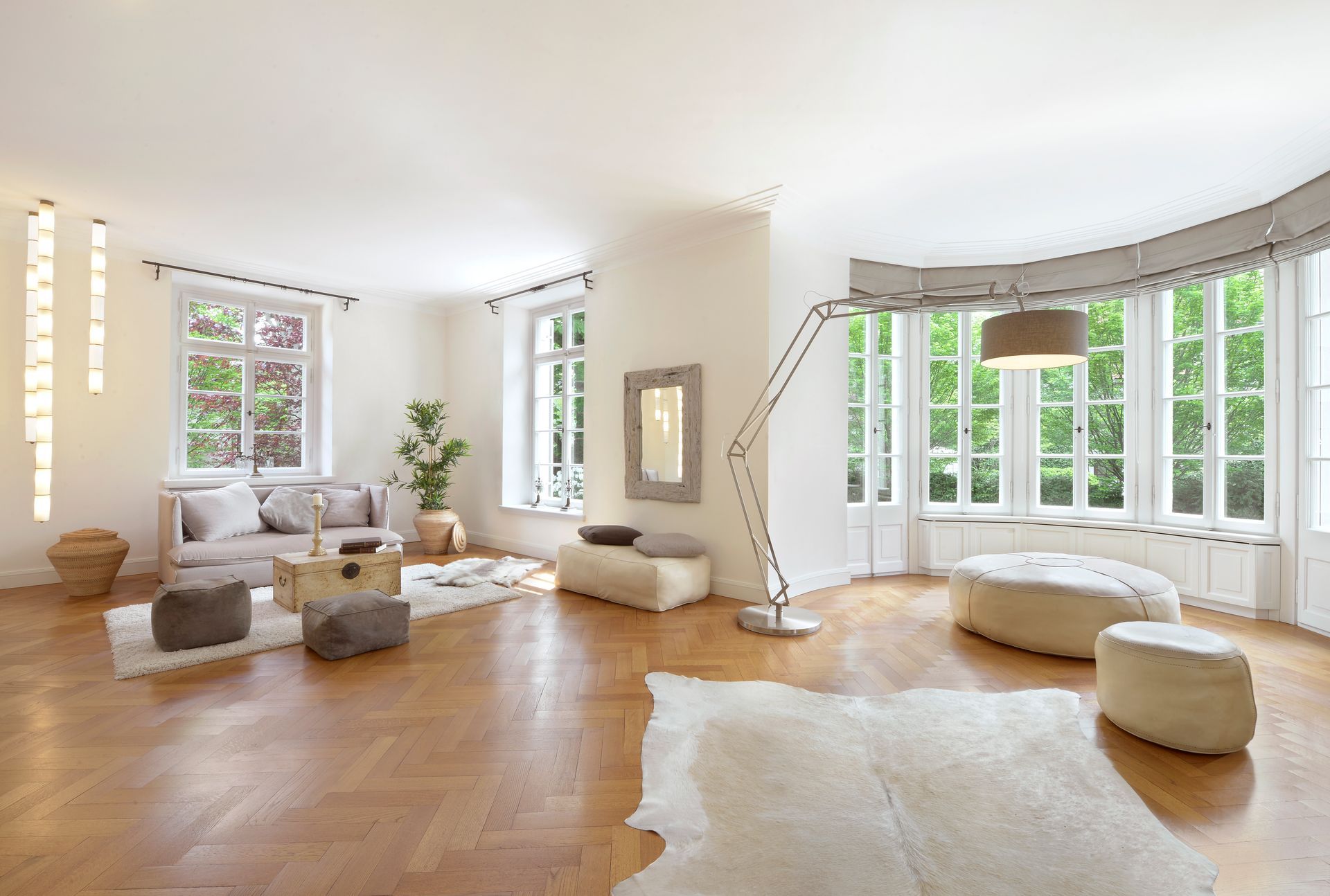 Spacious living room with natural light, hardwood floors, and neutral furnishings, including a sofa and large rug.