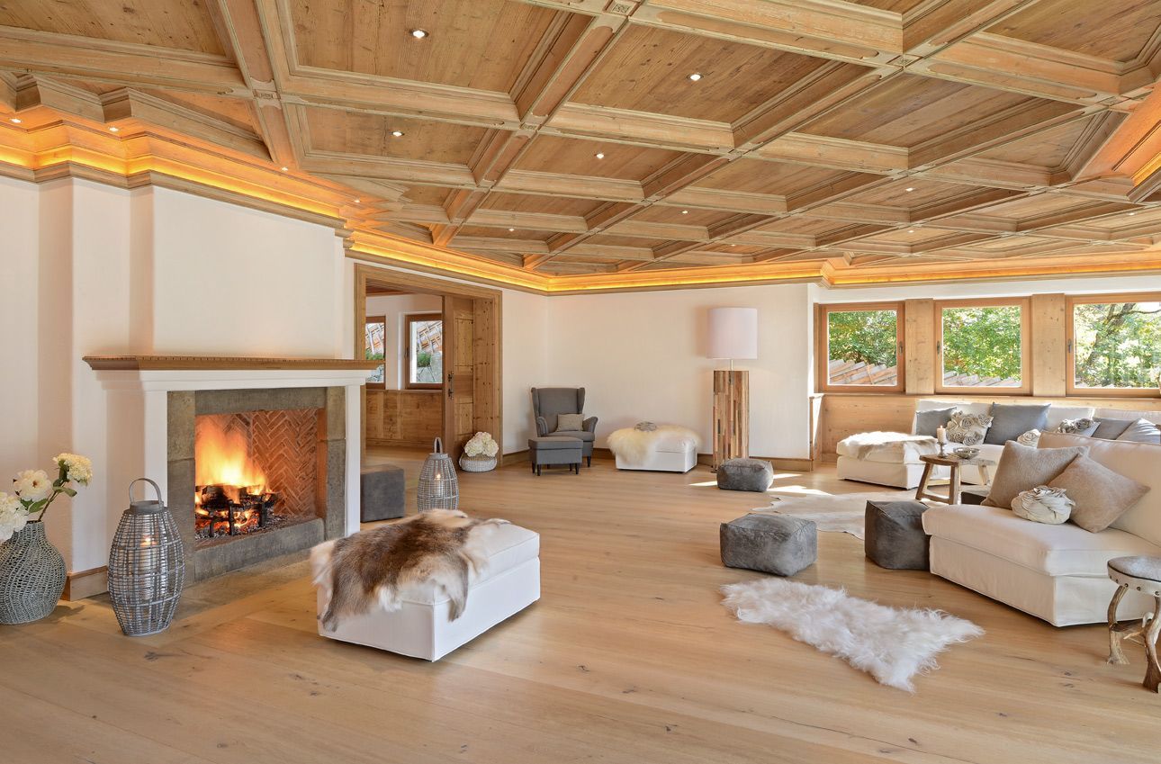 Cozy living room with fireplace, wood ceiling and floor, white furniture, and a window with a green view.